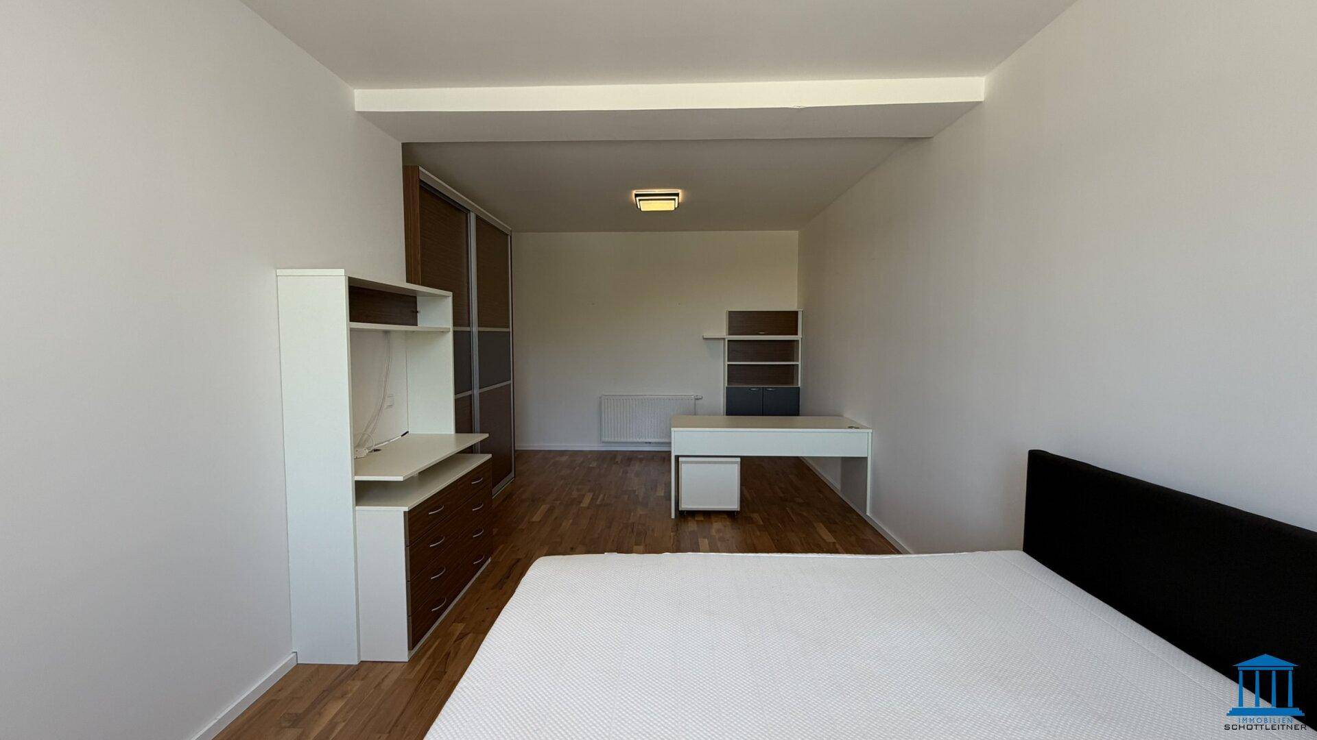 Geräumiges Schlafzimmer mit Holzboden, Schrank und Schreibtisch, hell durch das Fenster.
