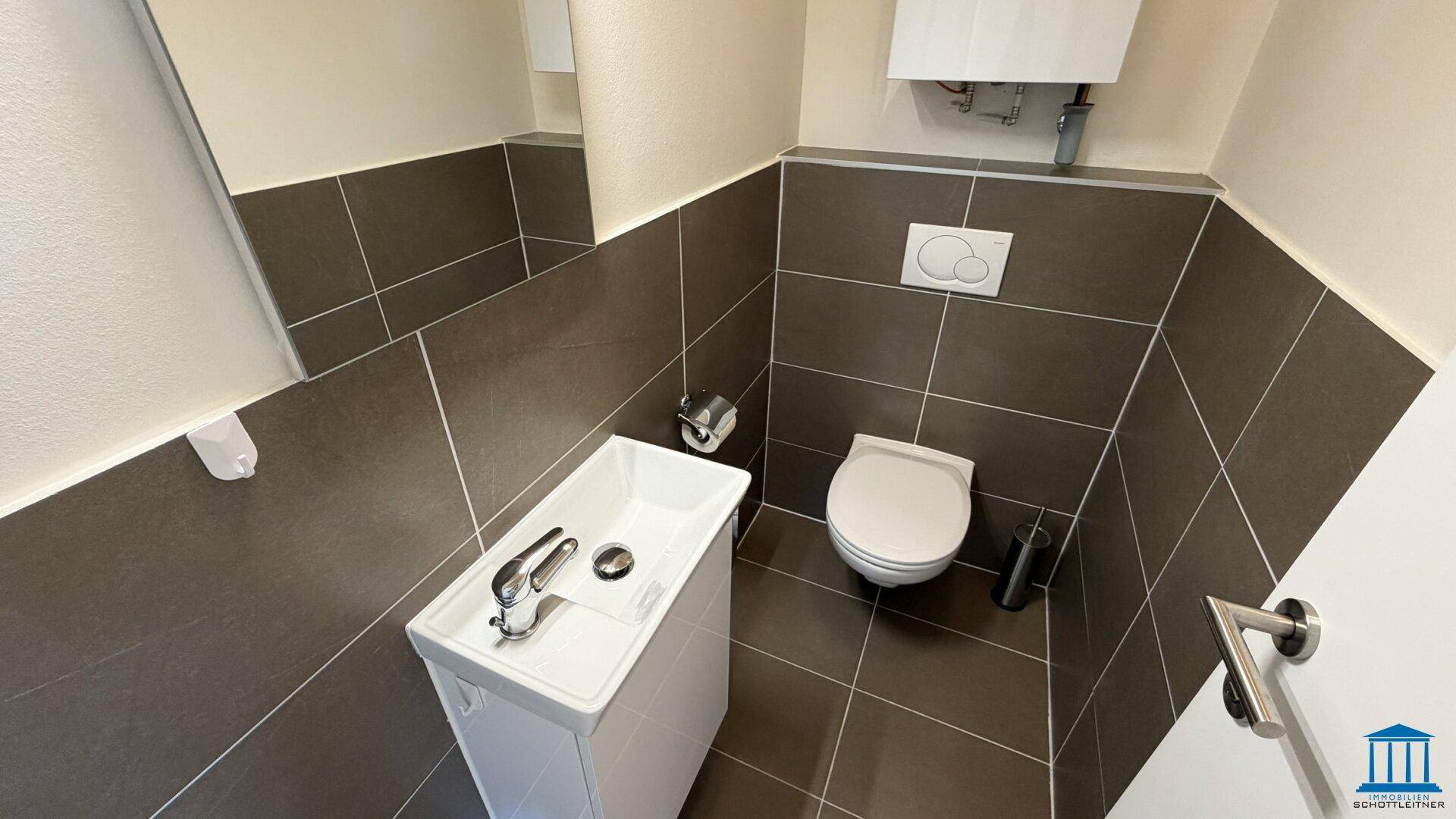 Kleines Gäste-WC mit modernen Fliesen, wandhängendem WC und kleinem Handwaschbecken.
