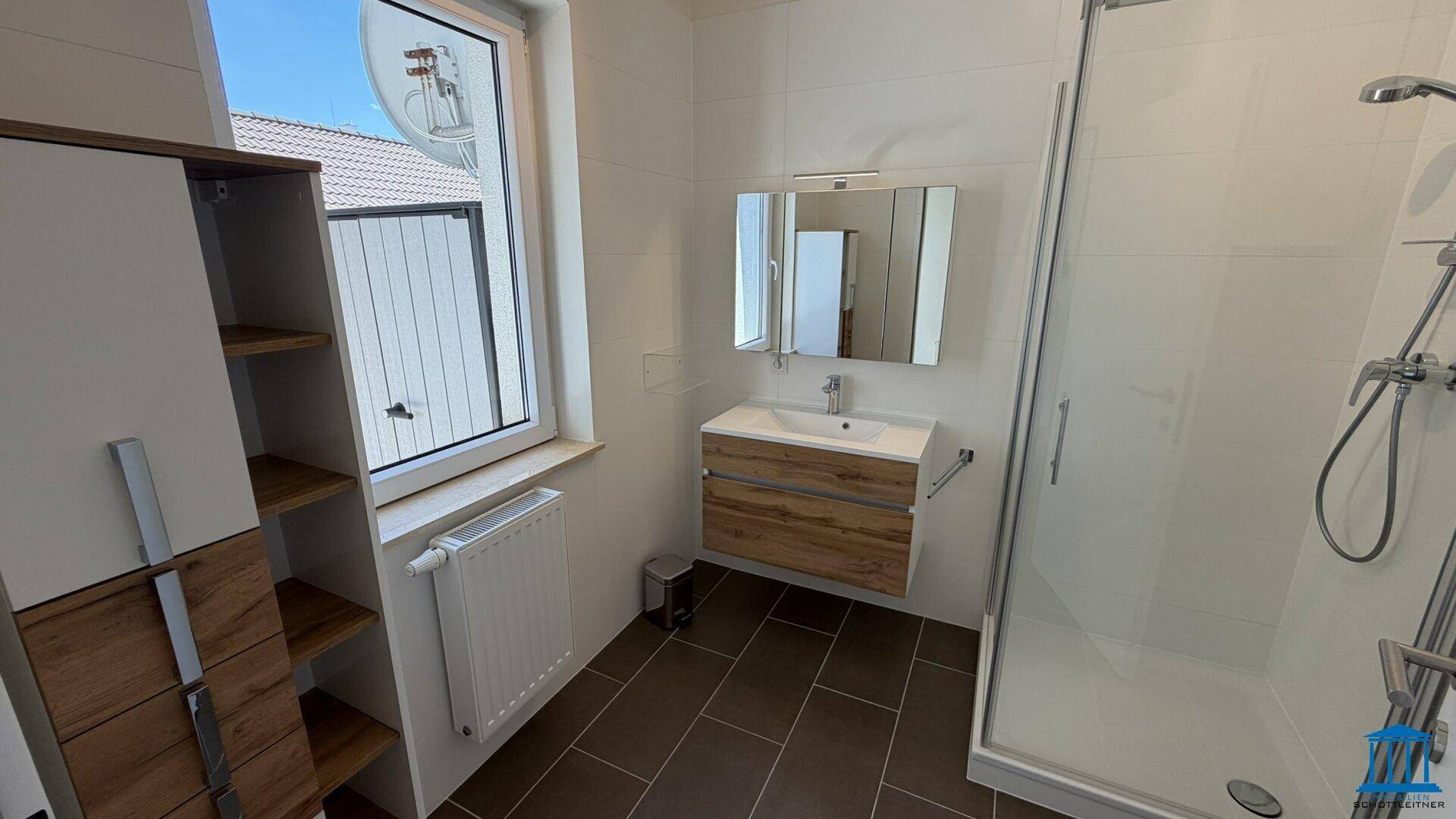 Modernes Badezimmer mit Dusche, Waschbeckenunterschrank und Fenster, gefliest in Weiß und Braun.