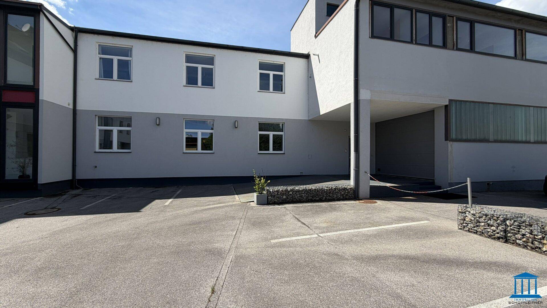 Rückseite eines modernen Gebäudes mit Parkplätzen und einer gepflegten Außenanlage.