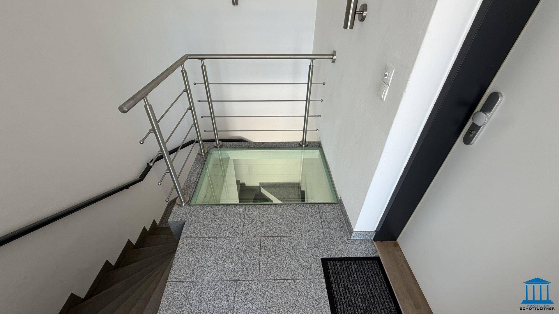 Treppenhaus mit Granitfliesen und Glasbodenplatte, die einen Blick nach unten ermöglicht.
