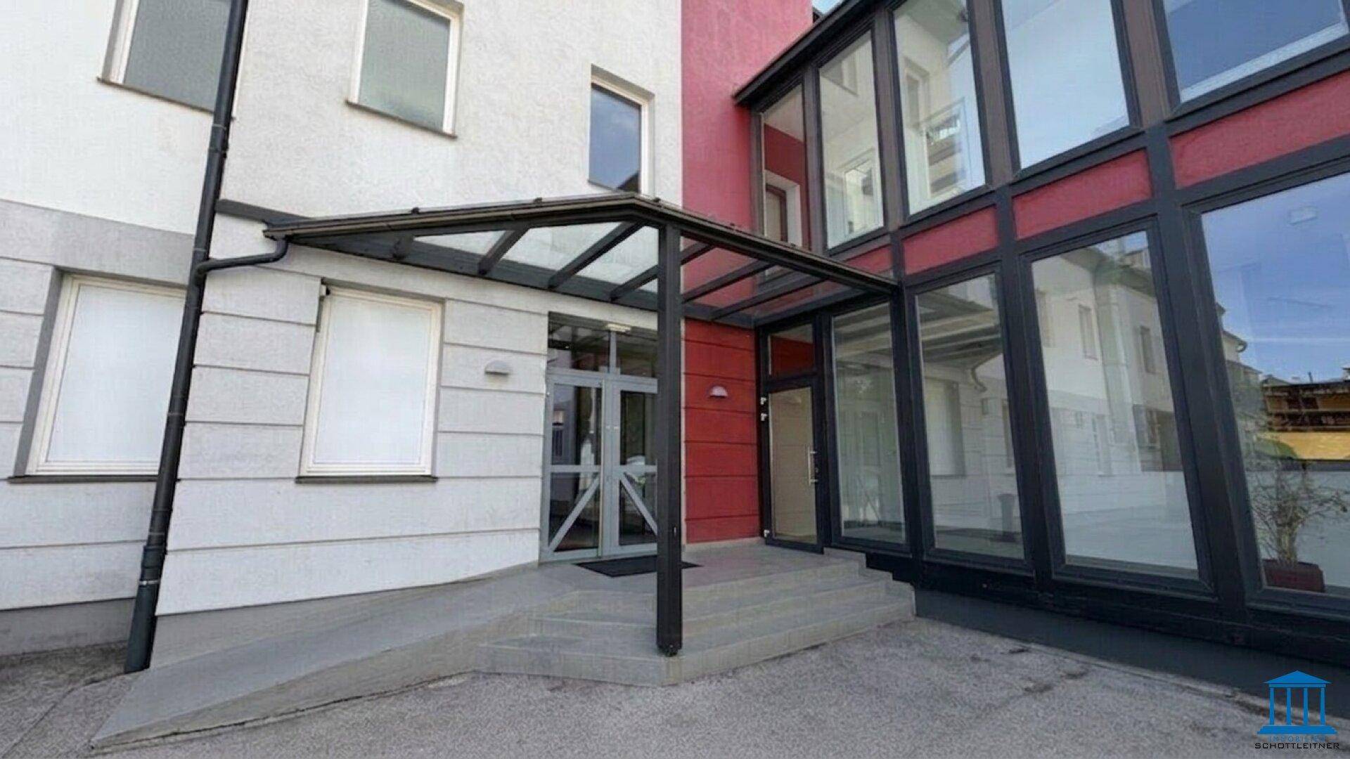 Eingangsbereich eines modernen Gebäudes mit Glasüberdachung und barrierefreier Rampe für einfachen Zugang.
