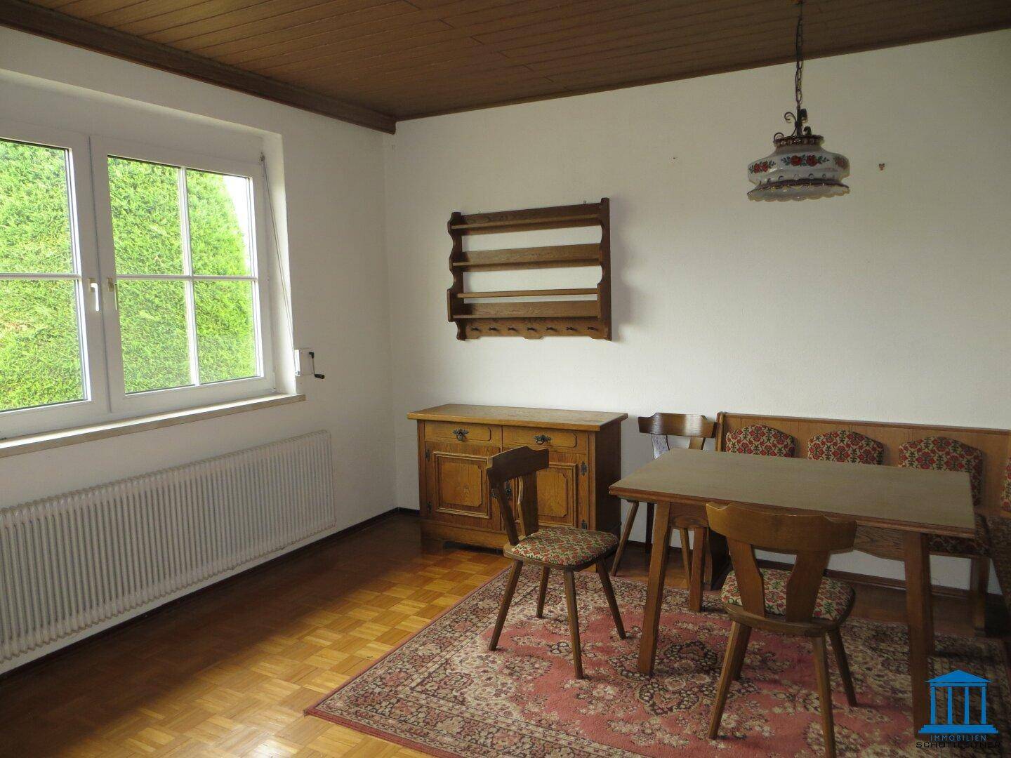 Essbereich mit Fensterblick ins Grüne, Heizkörper und einer Holzdecke, eingerichtet im traditionellen Stil.