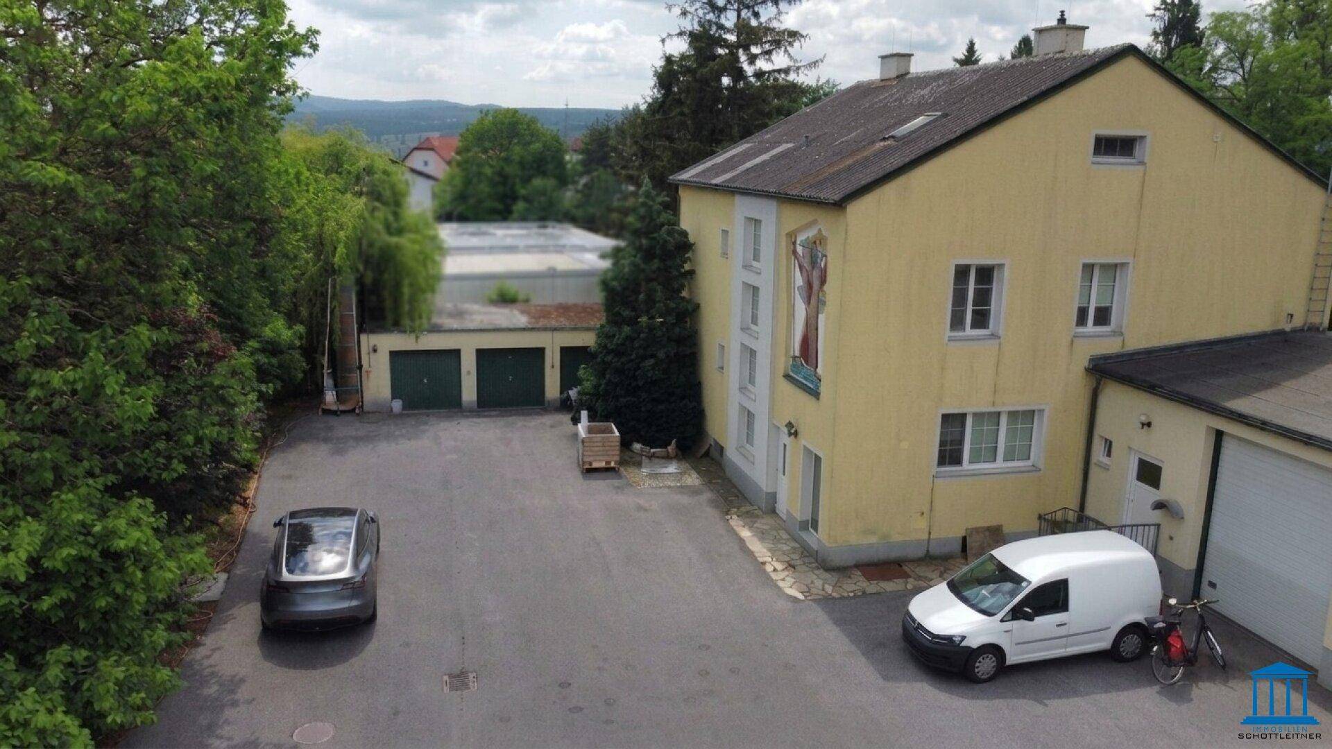 Außenansicht des gelben Gebäudes mit Parkplatz und Garagen, umgeben von Bäumen und mit Fernblick.