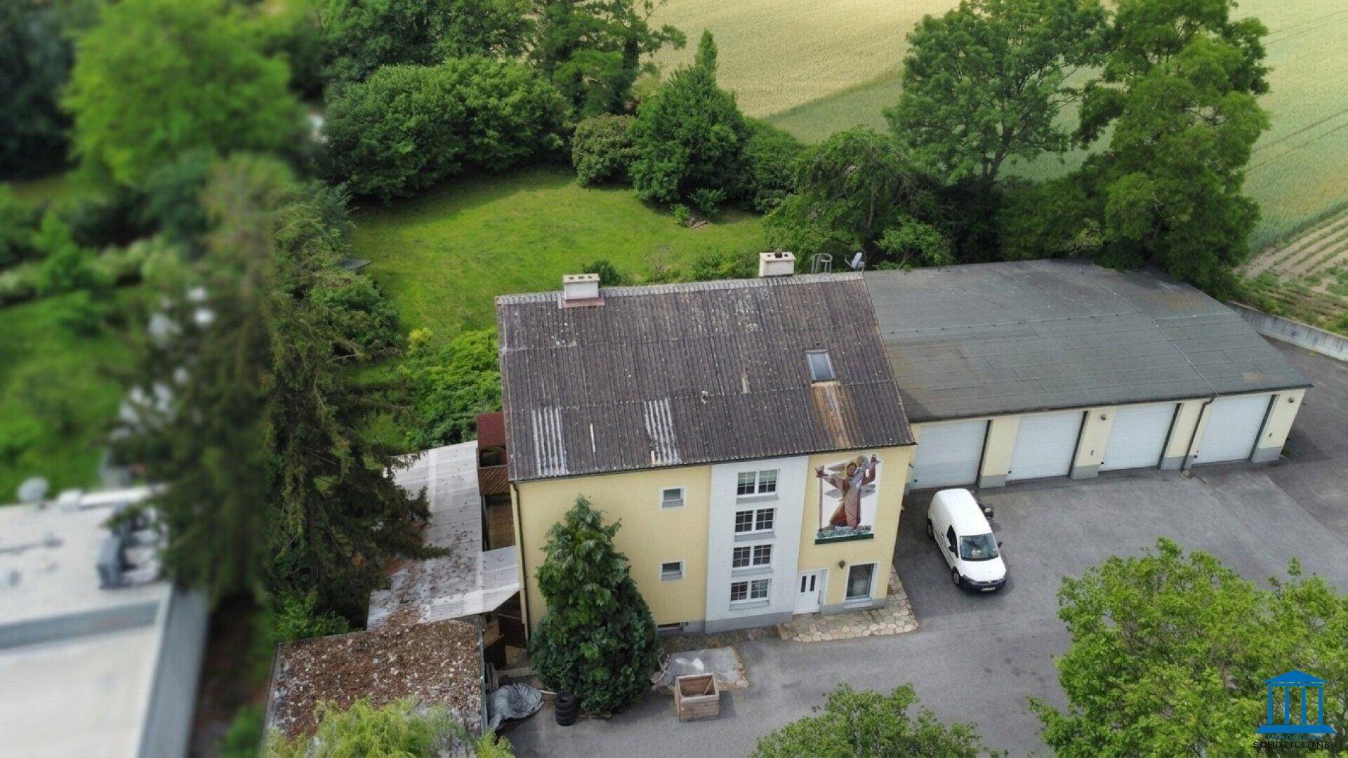 Nähere Luftaufnahme des gelben Gebäudes mit Wandgemälde und angrenzender Lagerhalle, umgeben von Natur.