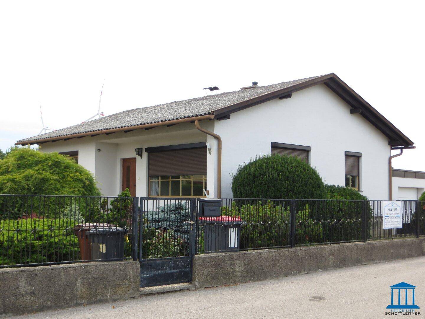 Seitenansicht des Einfamilienhauses von der Straße aus mit Zaun und Mülltonnen.