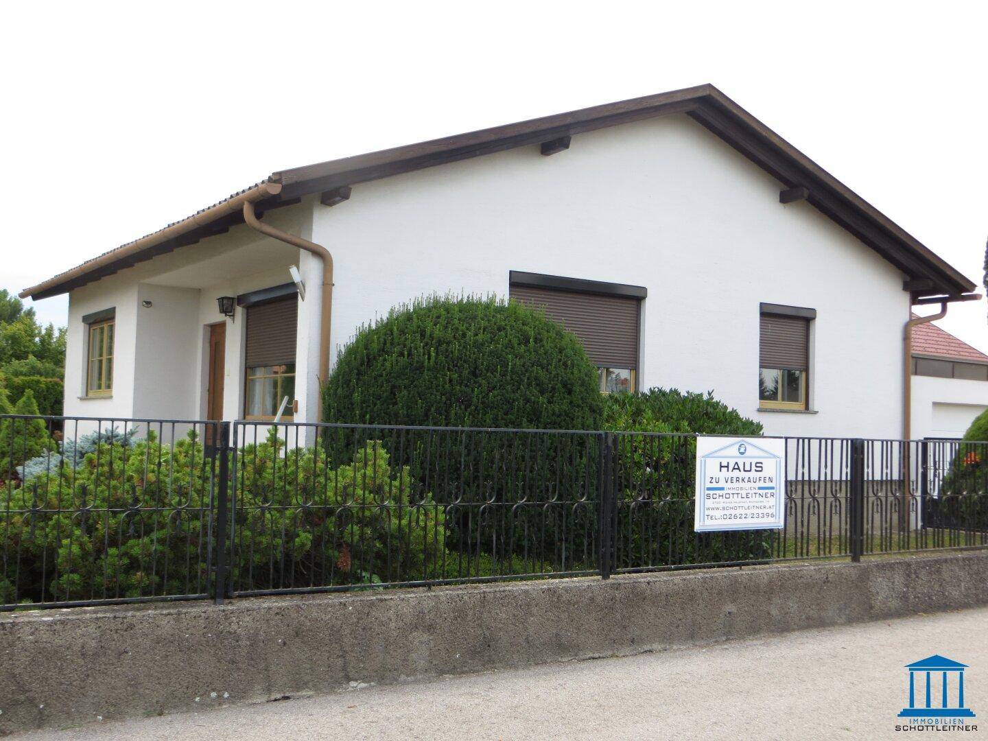 Das Einfamilienhaus von der Straßenseite mit einem Zaun und einem "Haus zu verkaufen"-Schild.