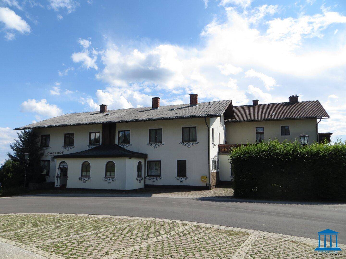 Ansicht des Gasthofs von der Straßenseite mit Parkplatz und gepflegter Hecke vor dem Gebäude.