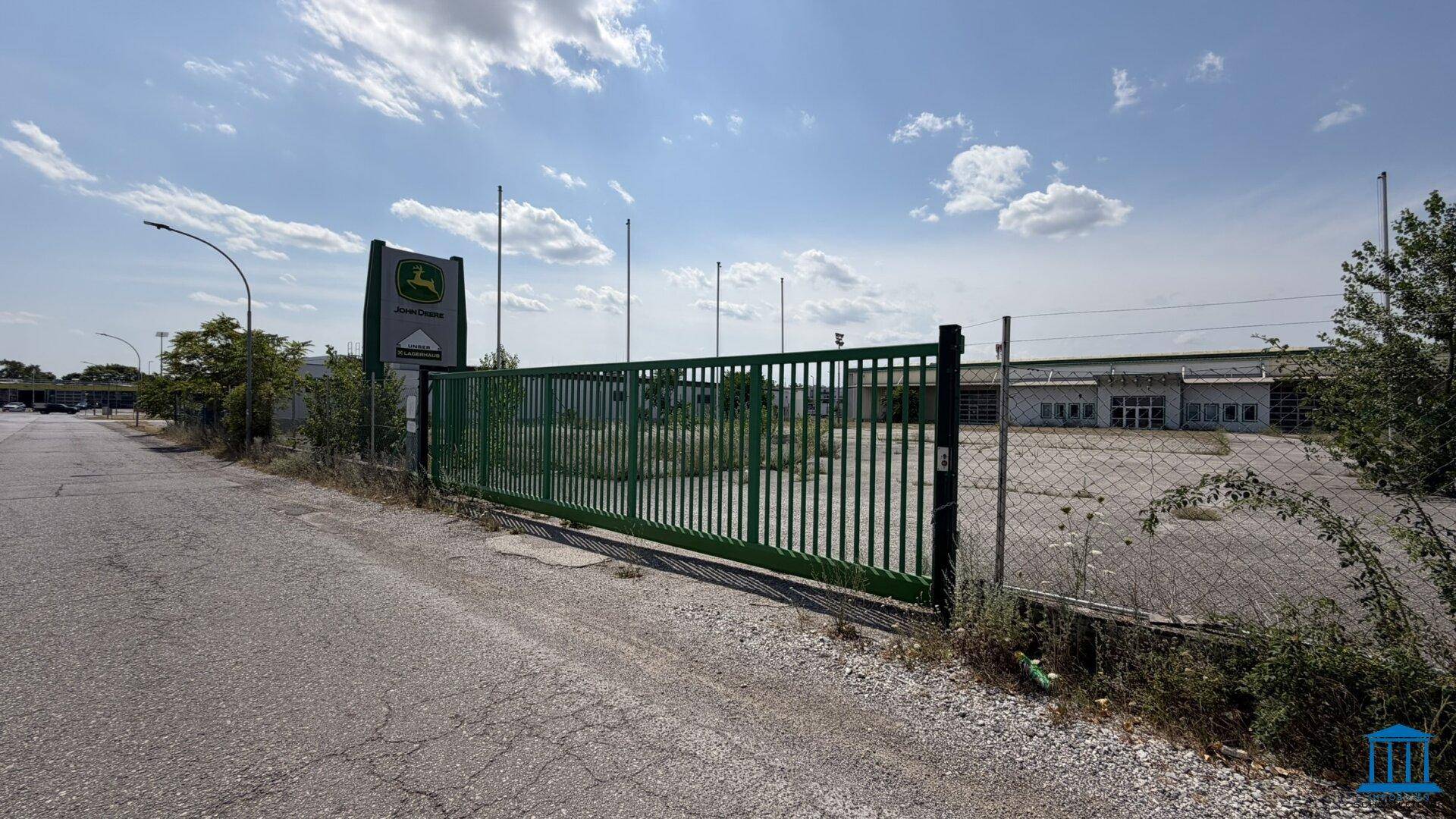 Grünes Eingangstor zum Grundstück mit einem John Deere Schild und der Zufahrt.
