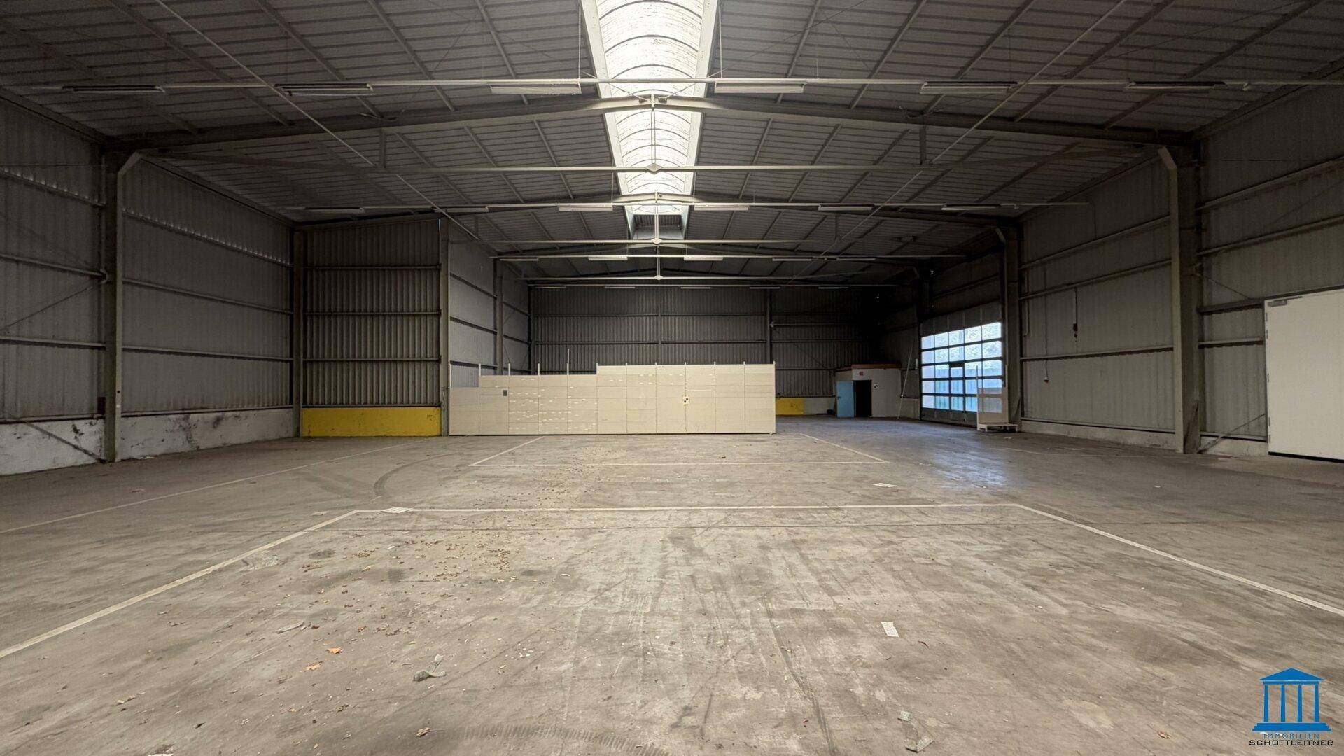 Große, leere Lagerhalle mit Betonboden, Wellblechwänden und Oberlichtern, bereit zur Nutzung.