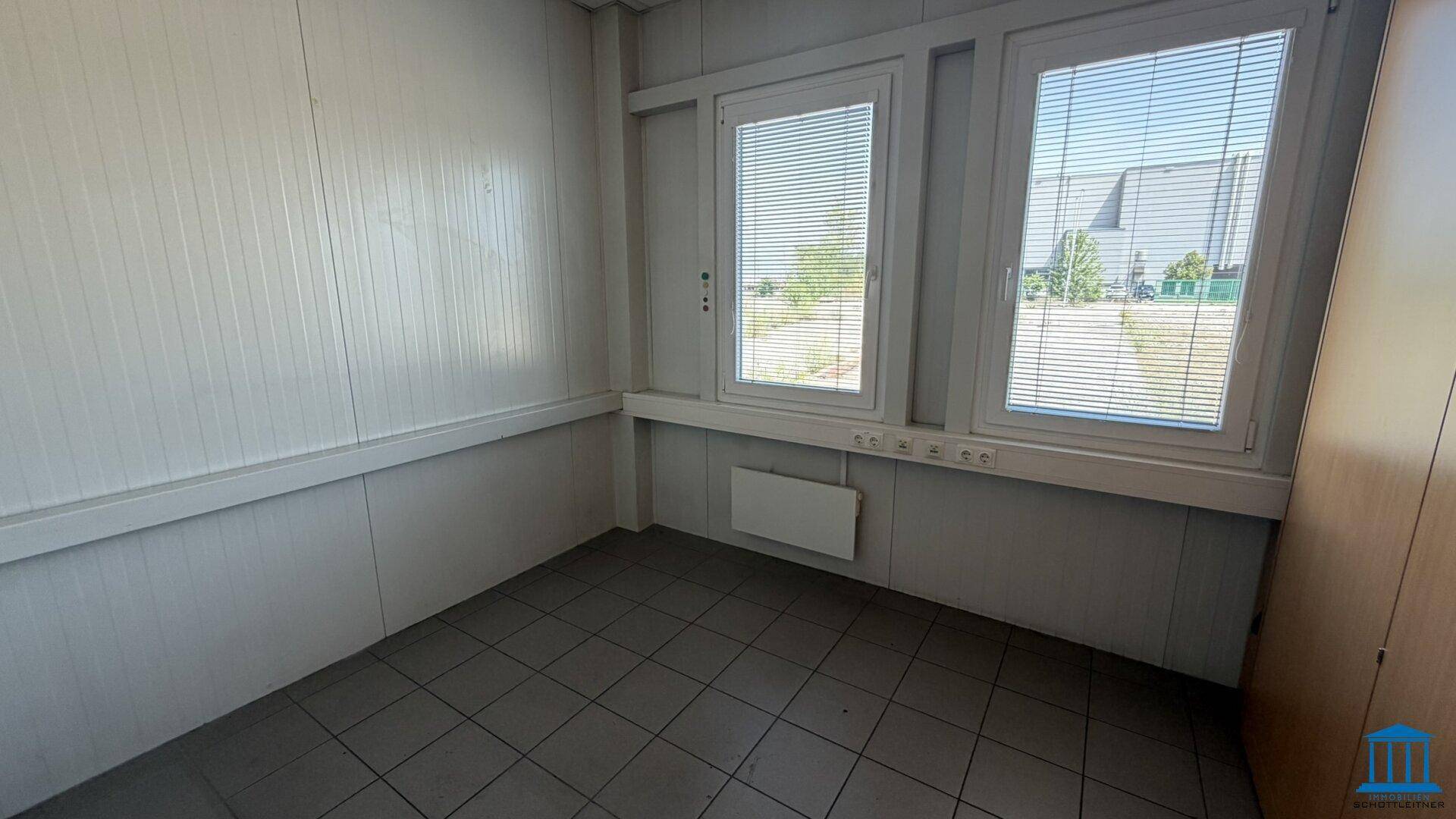 Kleineres Büro mit Fliesenboden und zwei Fenstern, die einen Blick nach draußen bieten.
