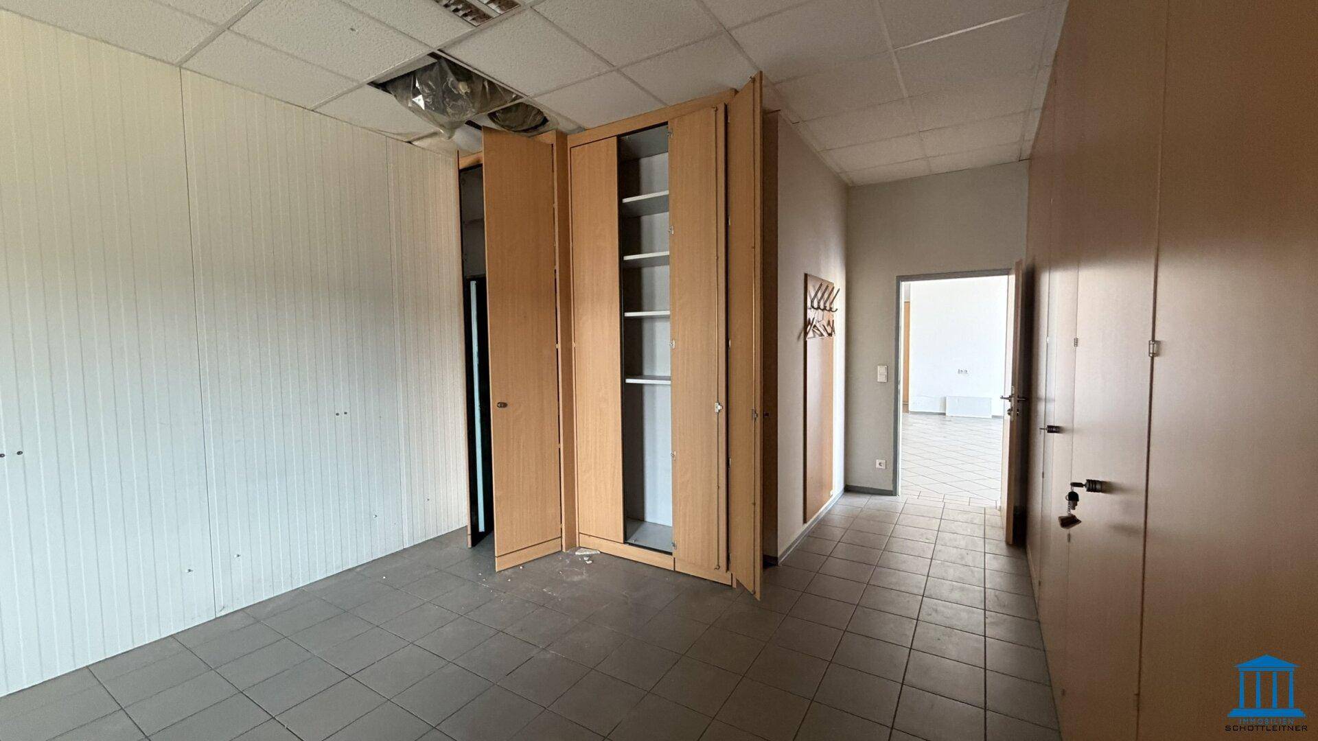 Bürogang mit offenen Einbauschränken, Fliesenboden und Durchgang zu weiteren Räumen.