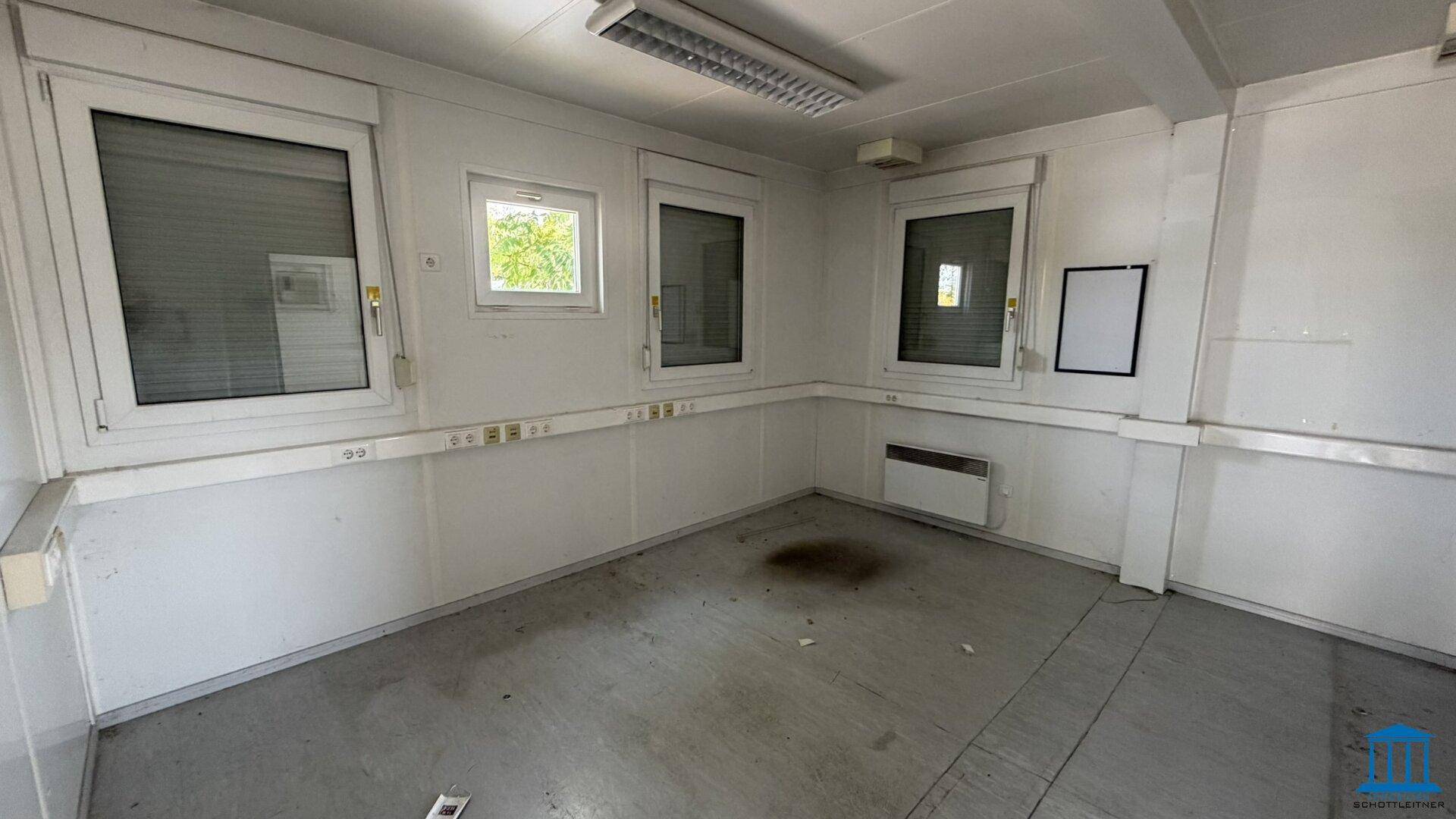 Innenraum eines Bürocontainers mit weißen Wänden, Fenstern mit Rollläden und einem strapazierfähigen Boden.