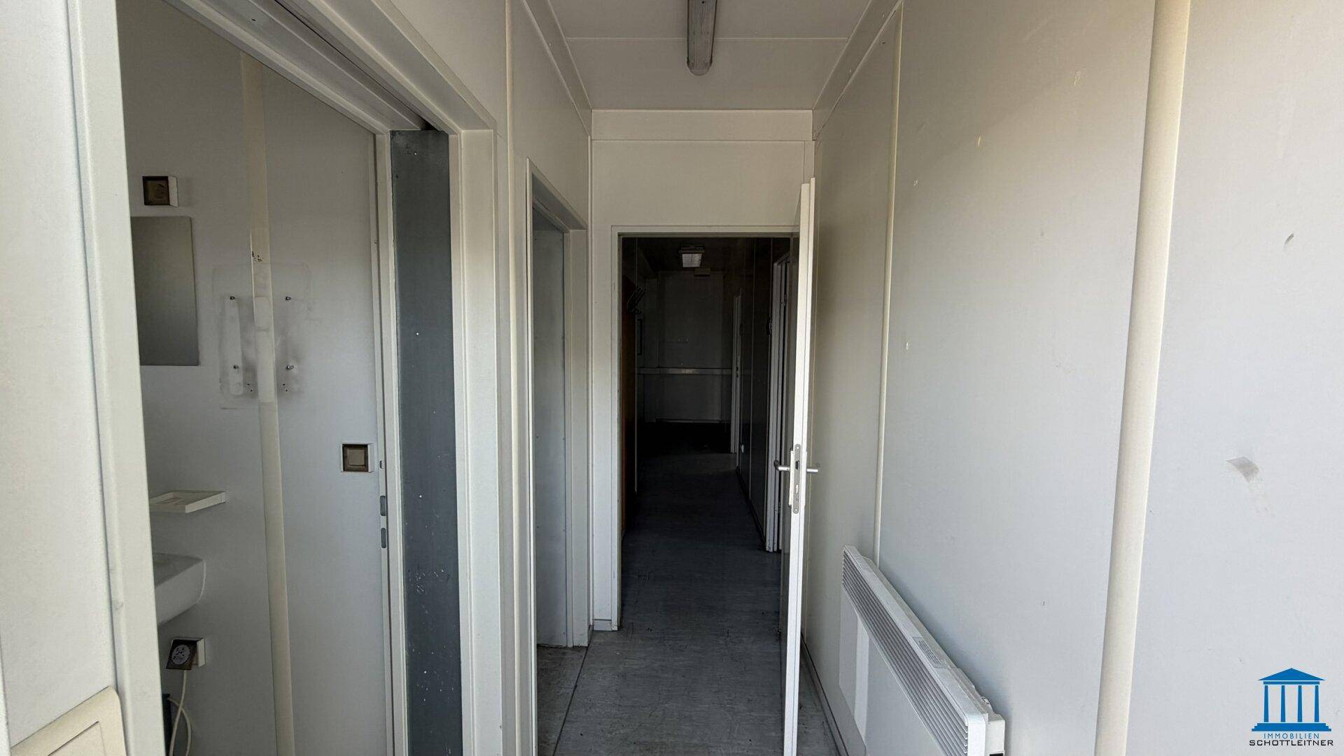 Flur in einem Containergebäude mit Vinylboden, weißen Wänden und mehreren Türen.