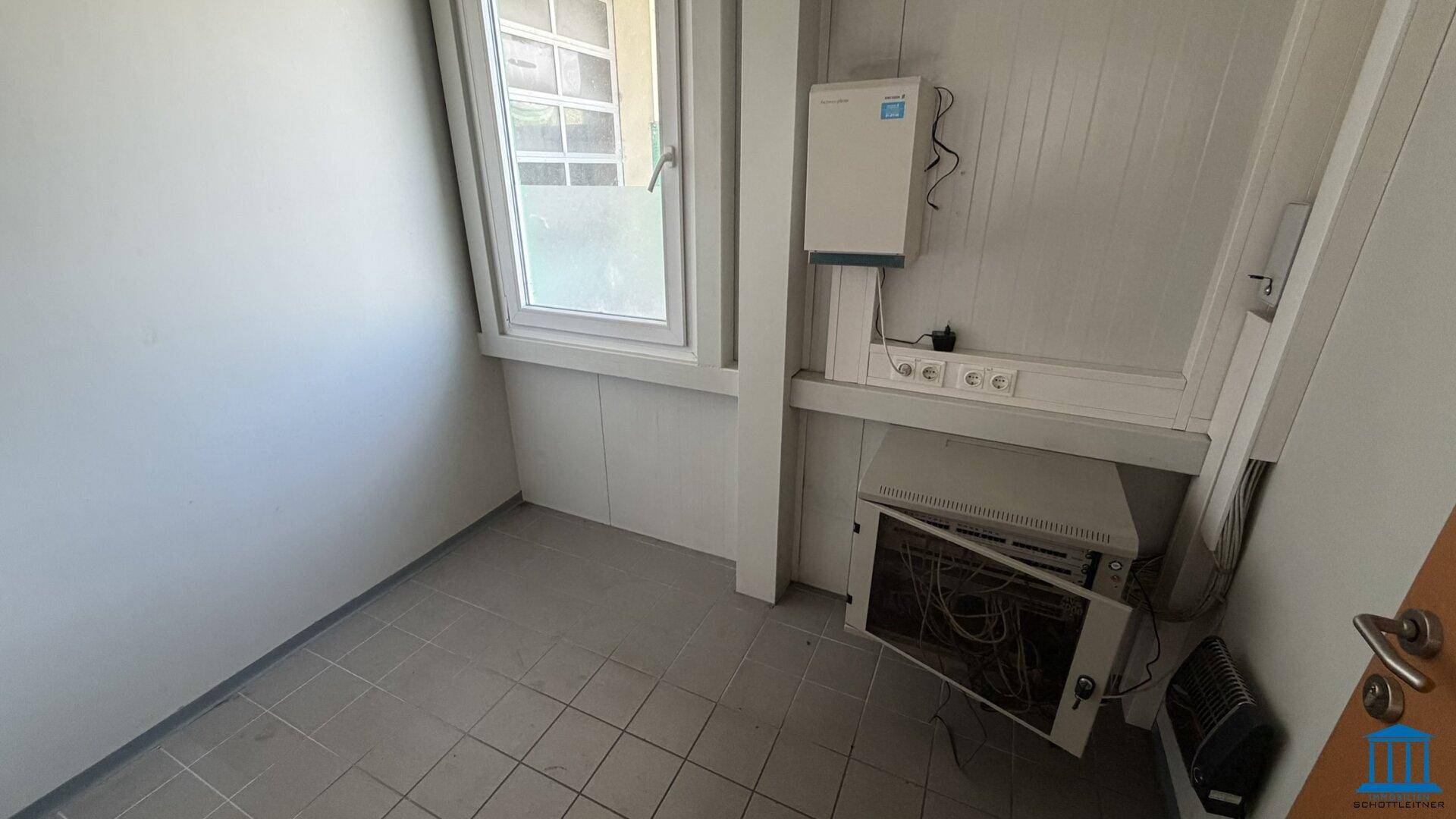 Kleiner Technikraum mit Fliesenboden, Fenster und einem Netzwerkschrank an der Wand.