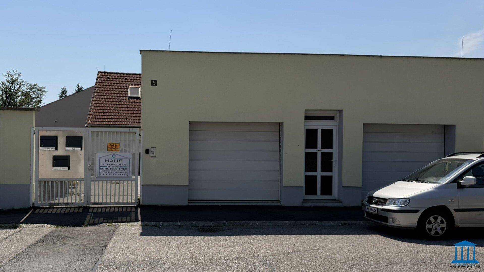 Vorderansicht des Gebäudes mit Garagentoren, Eingangstür und einem gepflegten Vorplatz.