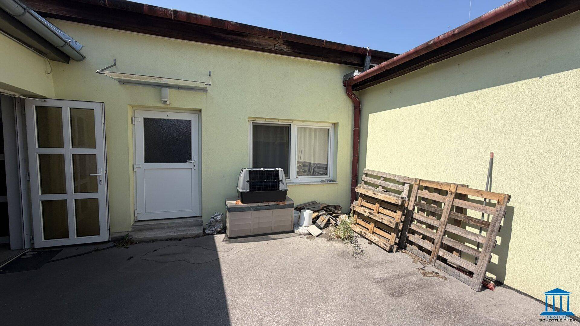 Hinterer Bereich des Gebäudes mit zwei Türen, einem Fenster und gelagerten Holzpaletten.