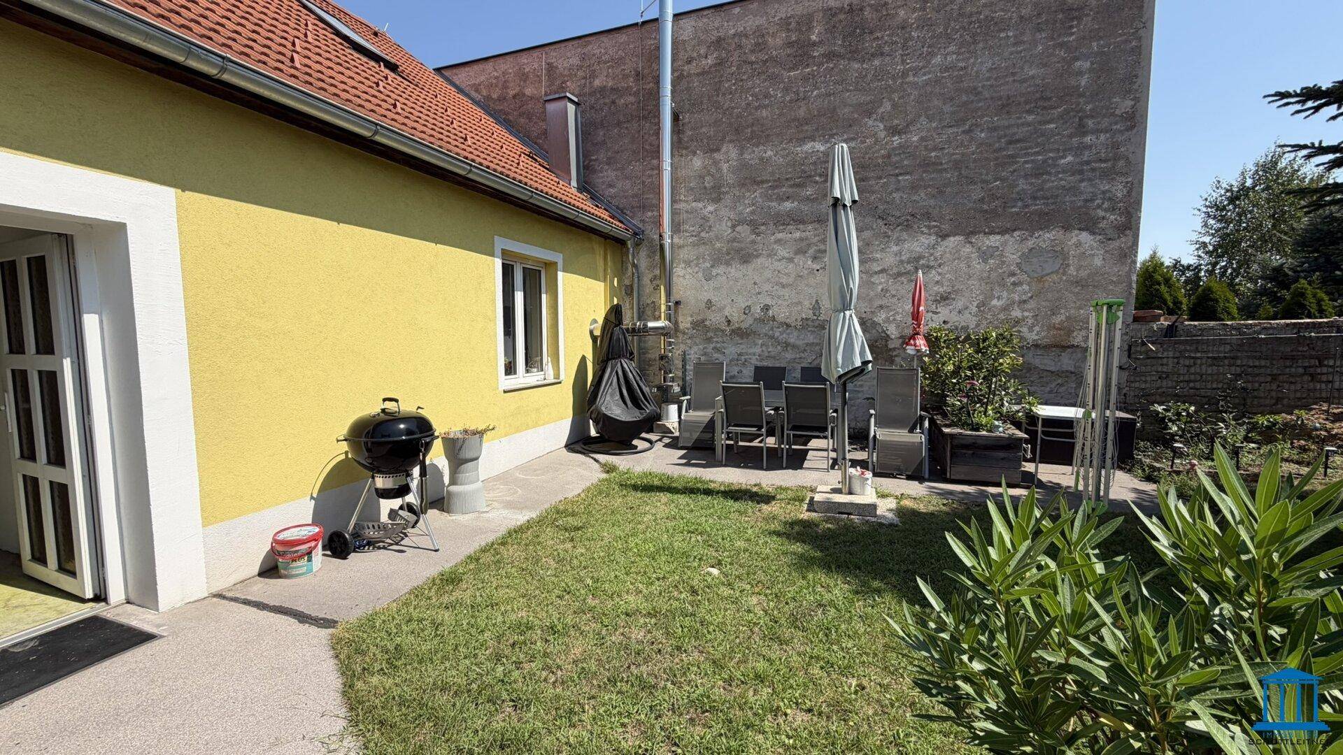 Kleiner Gartenbereich mit Rasenfläche, Grill und einer möblierten Sitzecke im Freien.