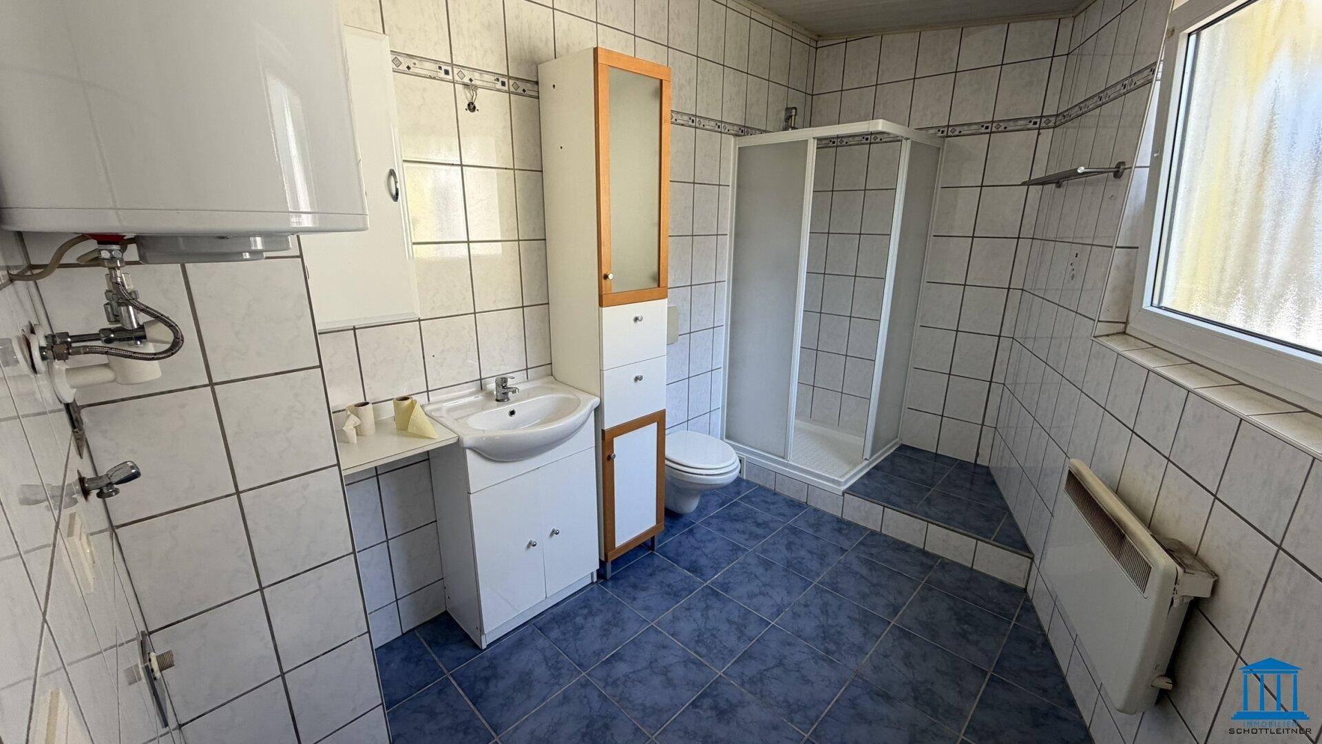 Badezimmer mit blauen Bodenfliesen, weißen Wandfliesen, Dusche und Waschbecken.