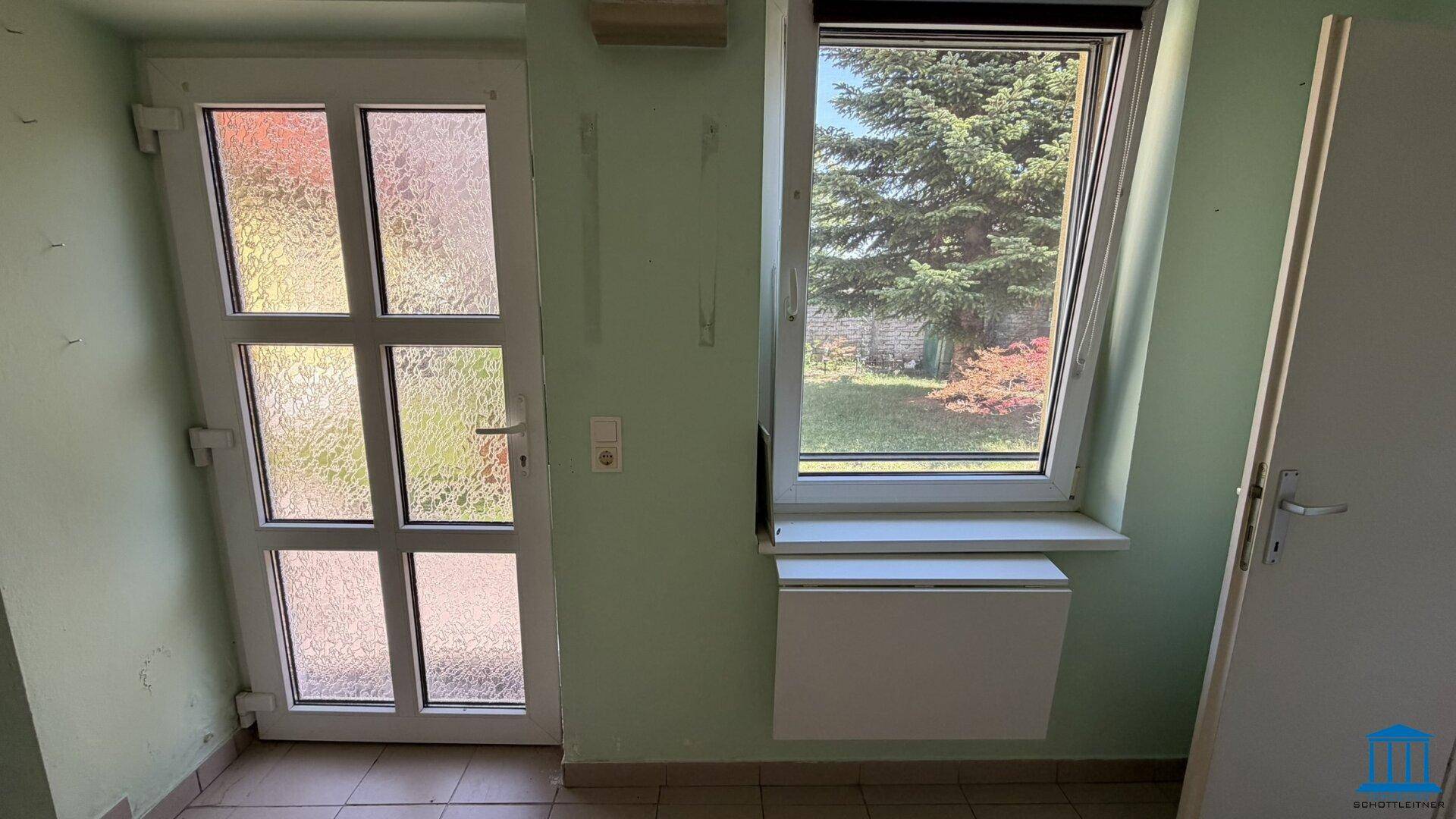 Heller Flurbereich mit einer Glastür, einem Fenster und Blick auf den grünen Garten.