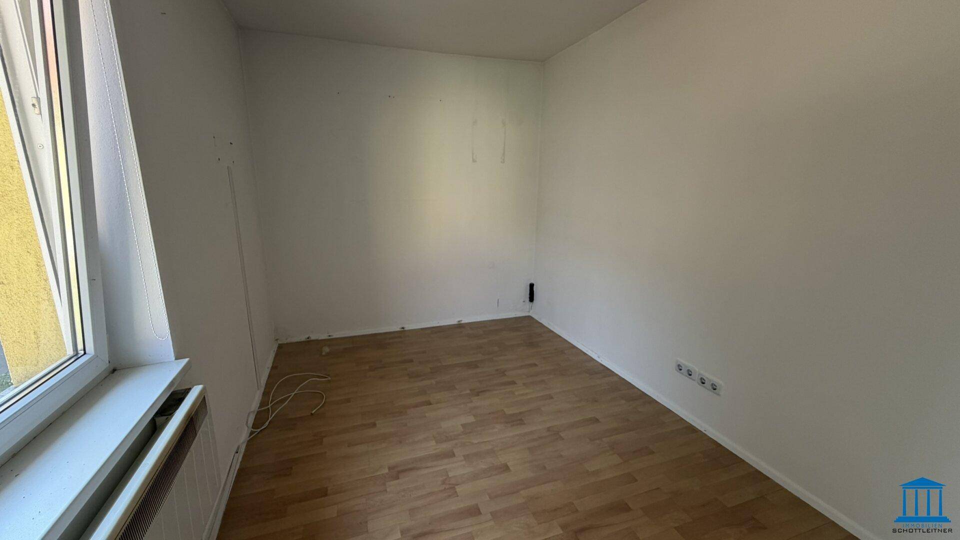 Helles Zimmer mit Laminatboden und weißen Wänden, bereit zur individuellen Gestaltung.