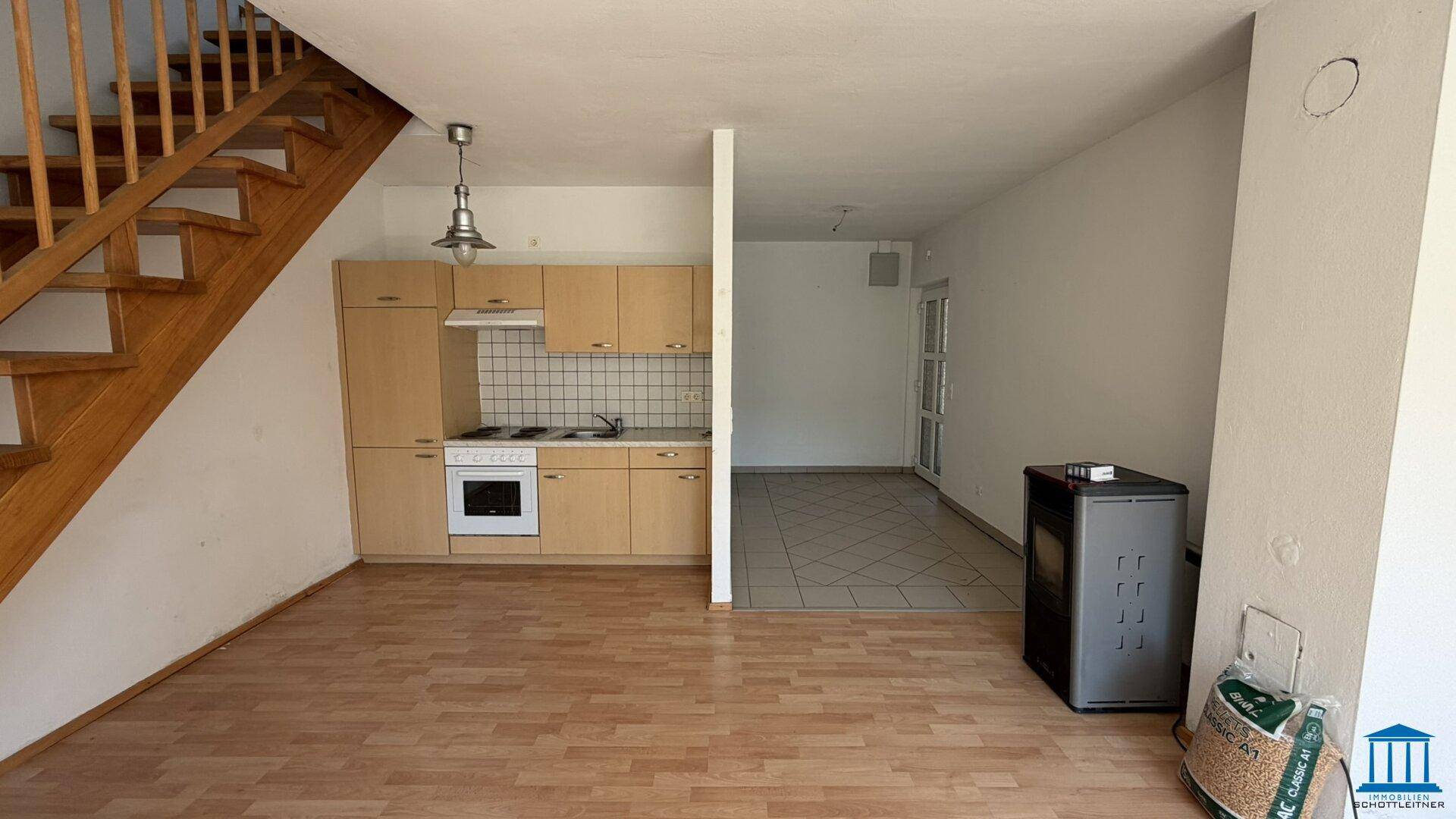 Offener Wohnbereich mit integrierter Küchenzeile, Laminatboden und einer Holztreppe.