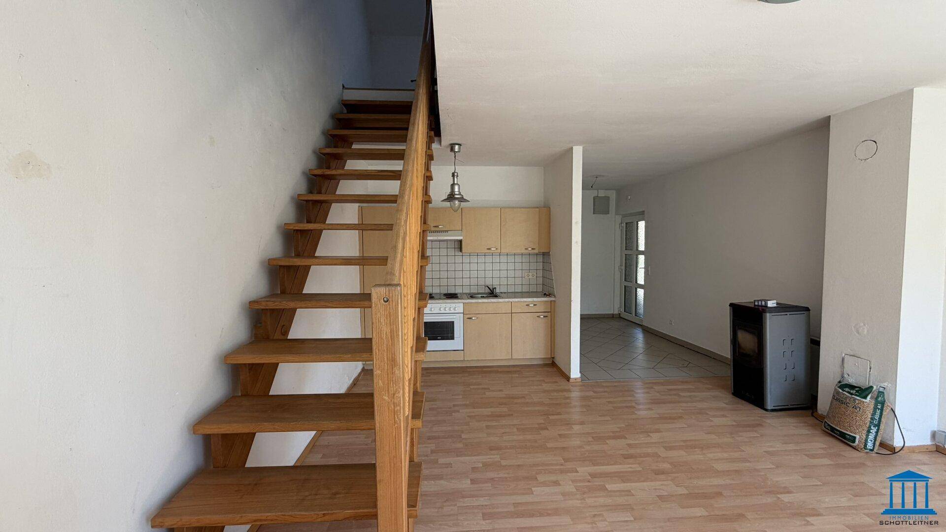 Geräumiger Wohnbereich mit offener Küche und markanter Holztreppe als zentrales Element.
