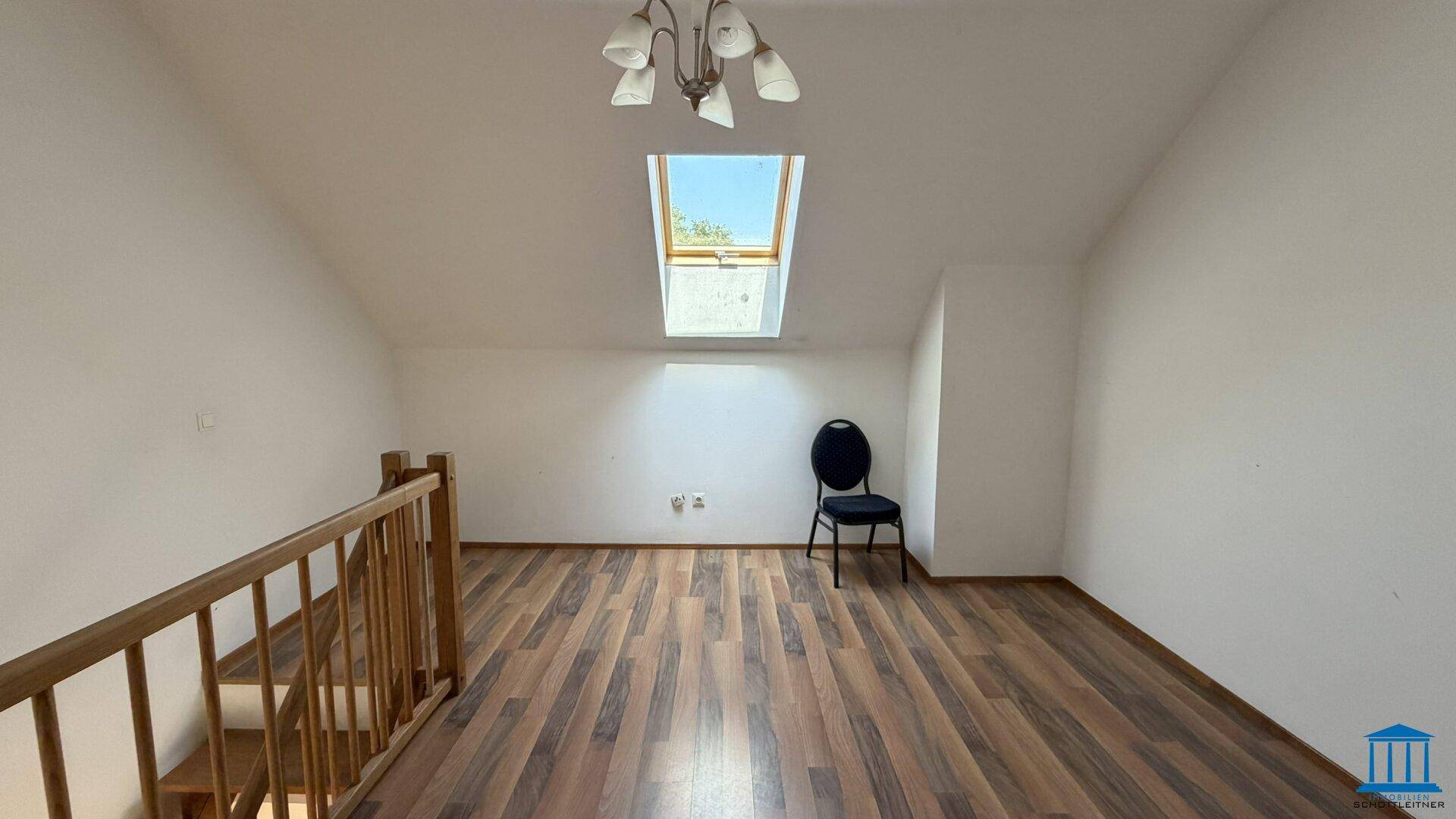 Helles Dachgeschosszimmer mit schrägen Wänden, Laminatboden und einem Dachfenster für Tageslicht.