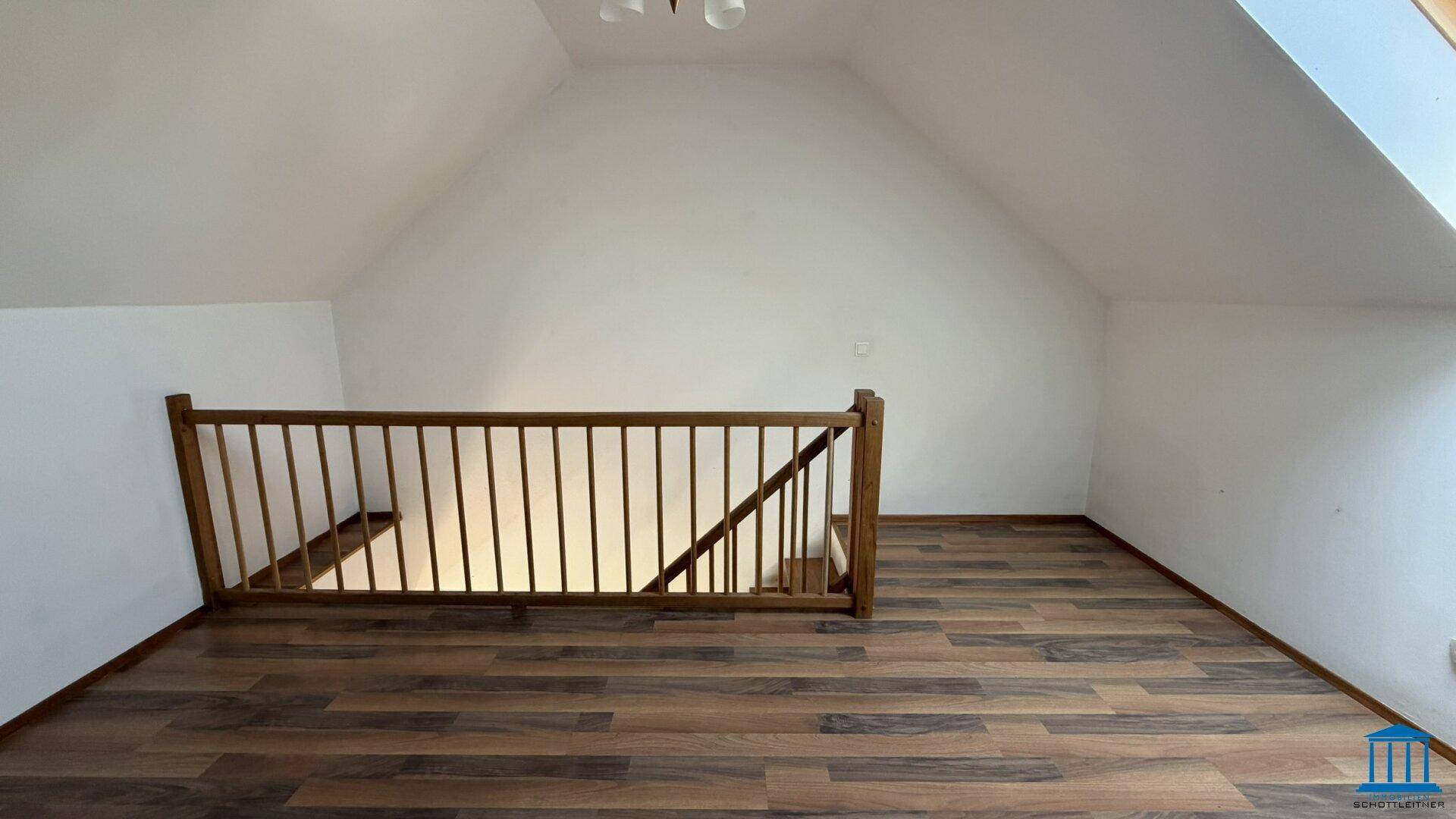 Geräumiges Dachgeschoss mit Laminatboden und einer Holzbrüstung, die den Treppenbereich abgrenzt.