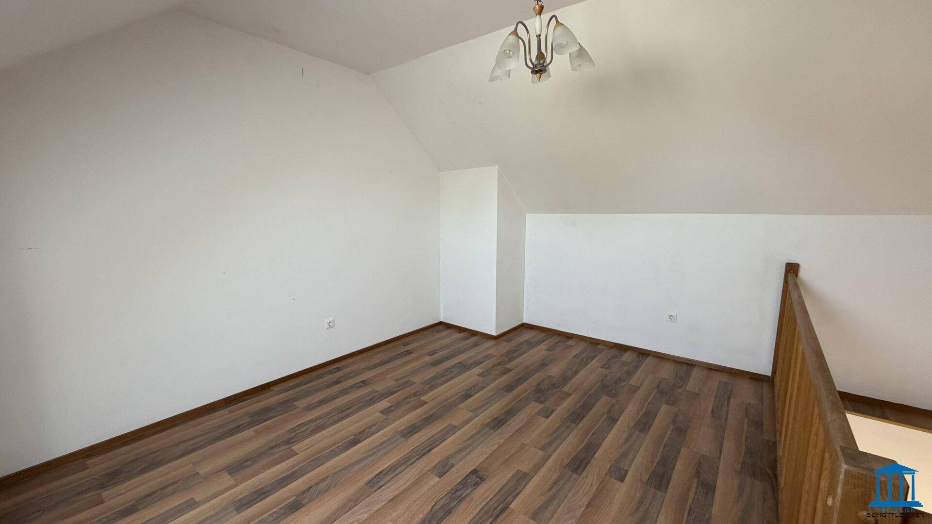 Dachgeschossraum mit Laminatboden, weißen Wänden und einer Holzbrüstung zur Treppe.