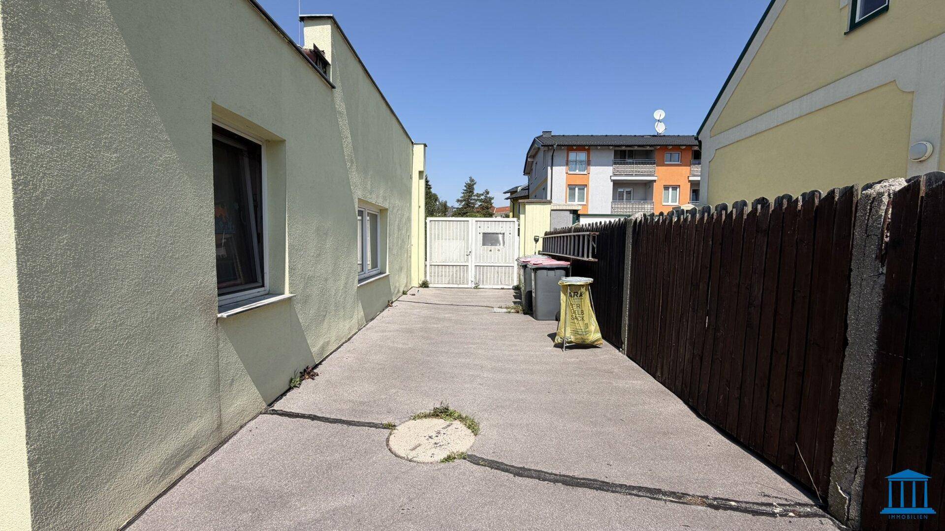 Schmaler gepflasterter Weg zwischen zwei Gebäuden, der zu einem hinteren Bereich führt.