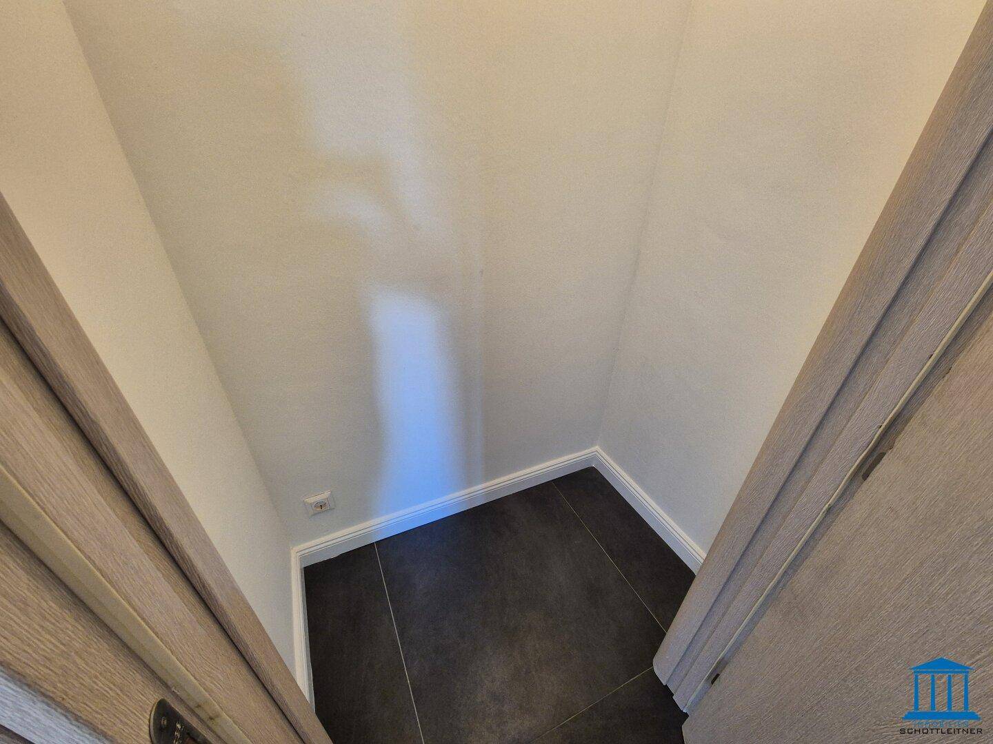 Praktischer Abstellraum mit dunklem Fliesenboden und weißen Wänden.