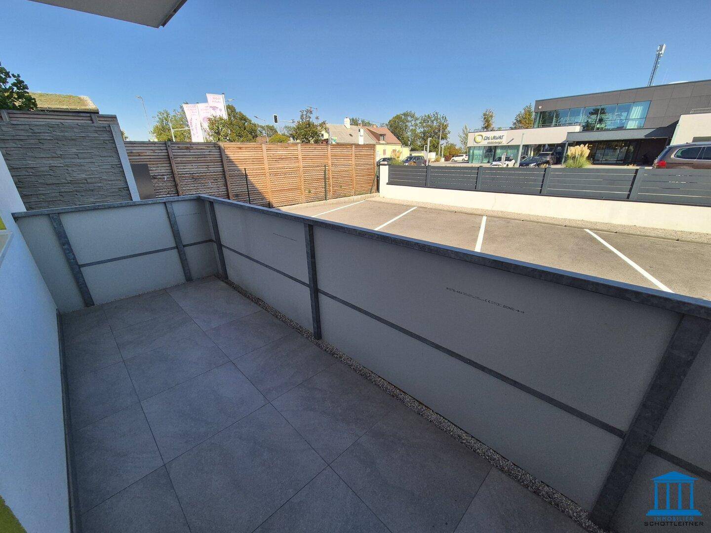 Moderne Terrasse mit Fliesenboden und Blick auf den Parkplatz und die Straße.
