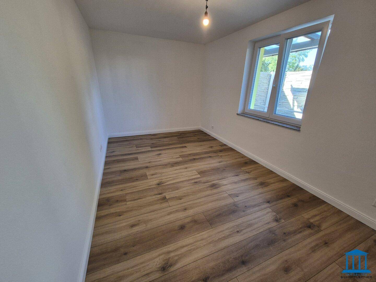Freundliches Schlafzimmer mit Laminatboden und einem großen Fenster für viel Tageslicht.
