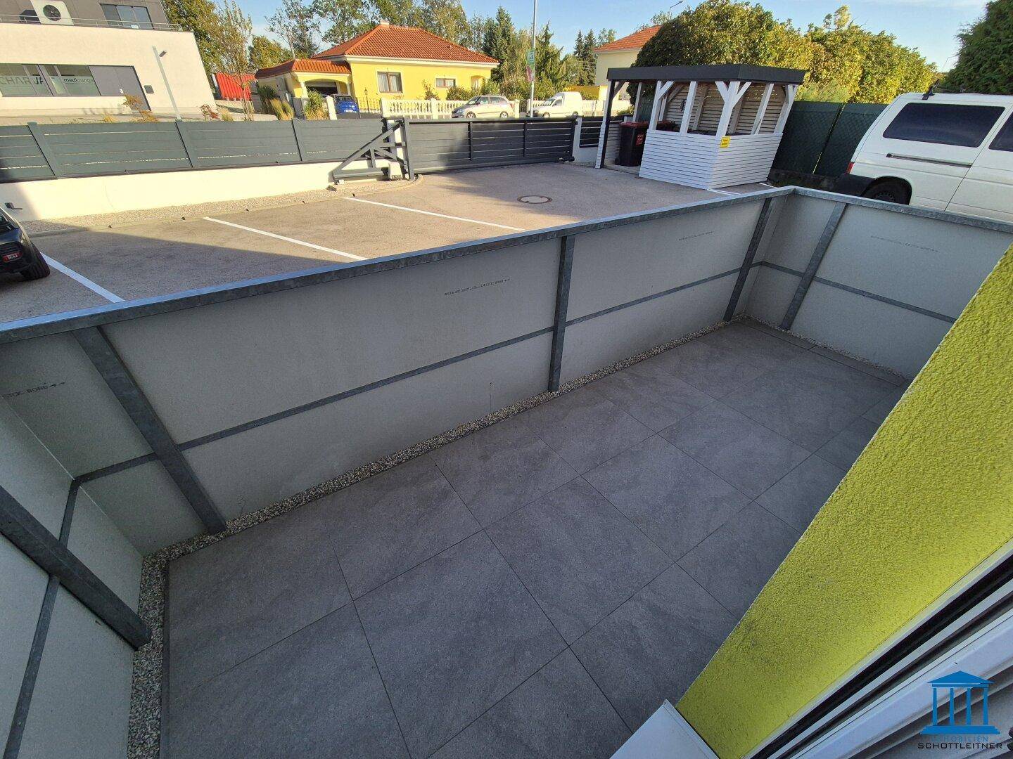 Private, geflieste Terrasse mit niedrigen Wänden und Blick auf den Parkplatz und die Umgebung.