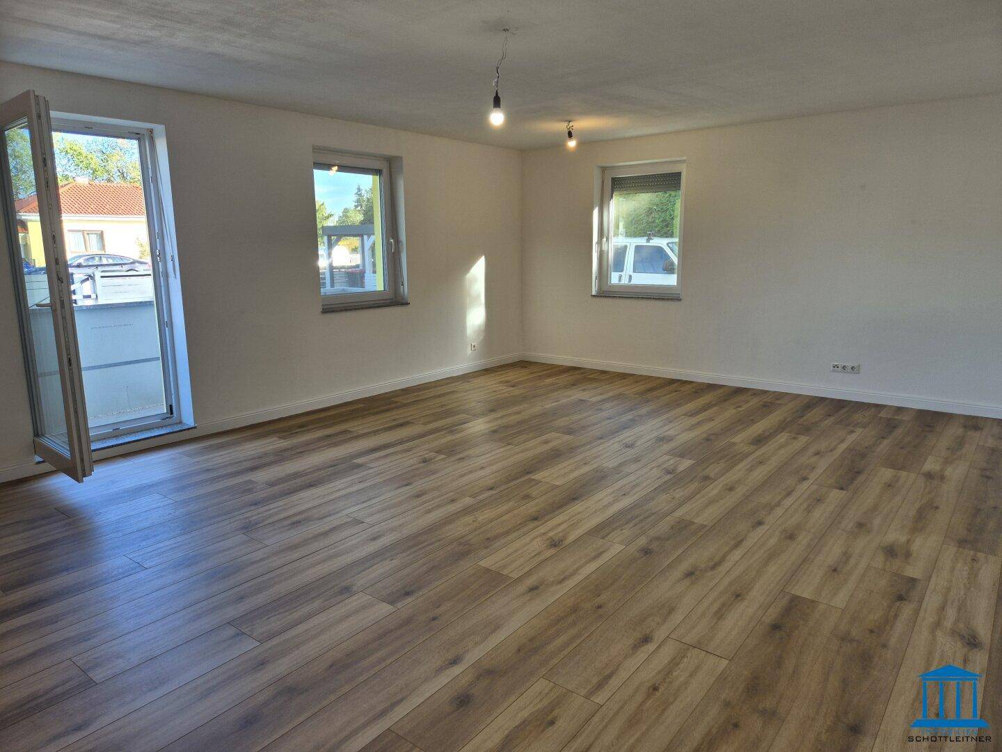 Geräumiges, helles Wohnzimmer mit Laminatboden, großen Fenstern und direktem Zugang nach draußen.