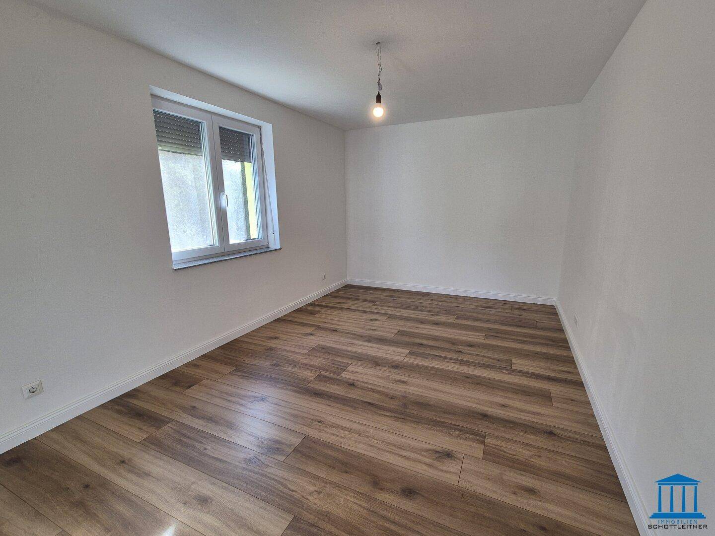 Helles Schlafzimmer mit Laminatboden, weißen Wänden und einem Fenster mit Rollladen.