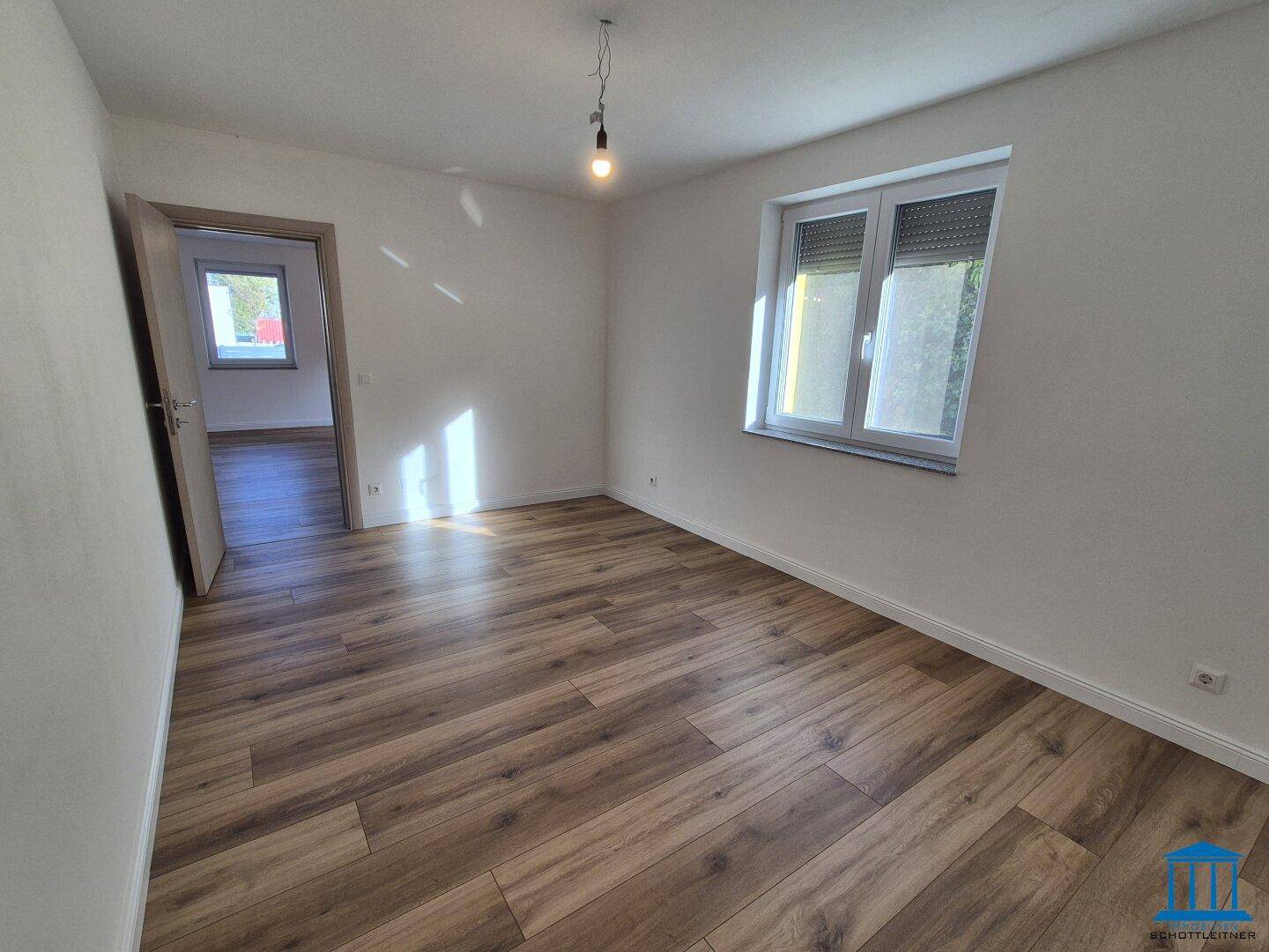 Geräumiges Schlafzimmer mit Laminatboden und Zugang zu einem weiteren Zimmer, gut beleuchtet.