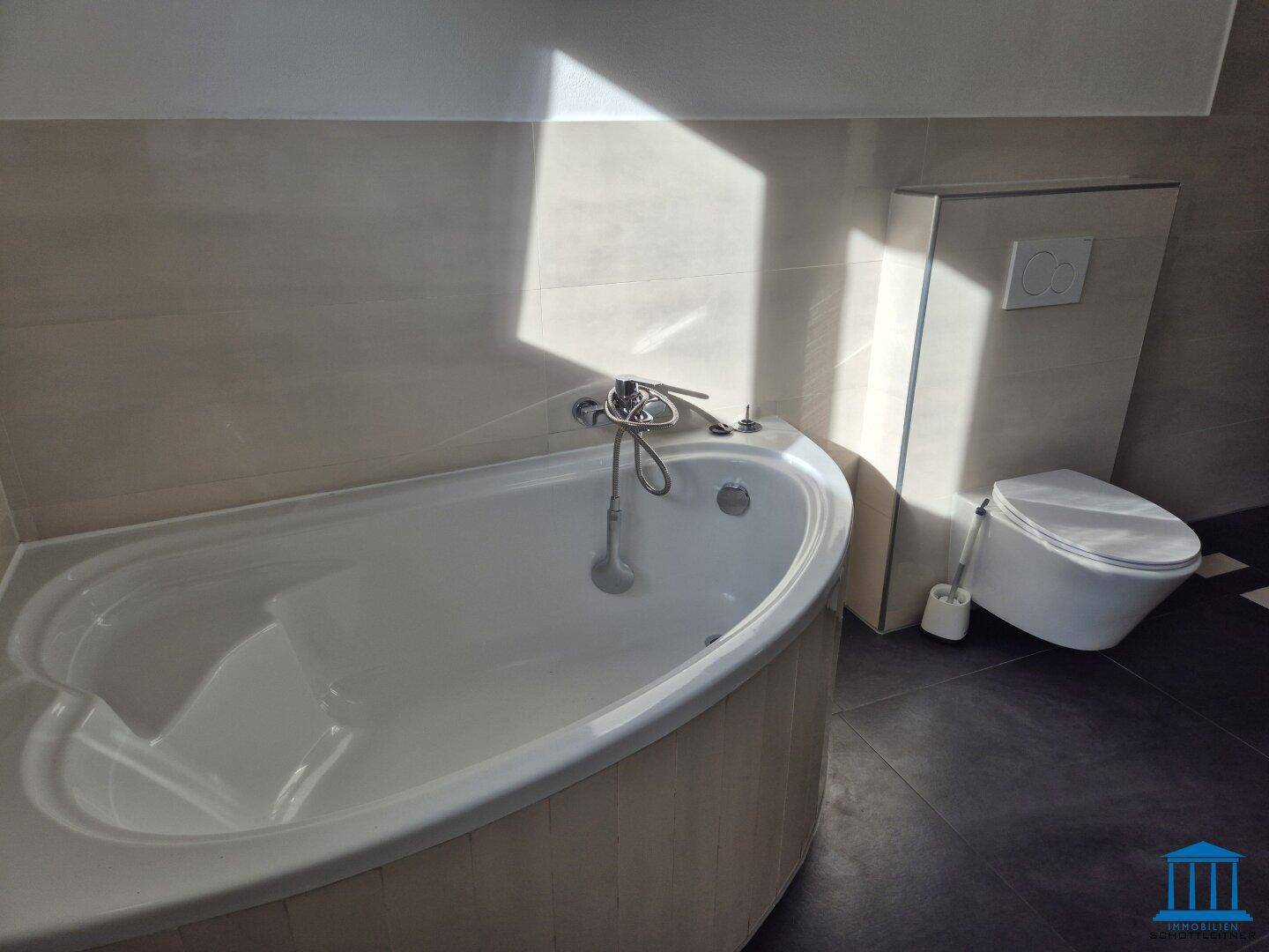 Eckbadewanne und wandhängendes WC in einem modernen Badezimmer mit hellen Fliesen.