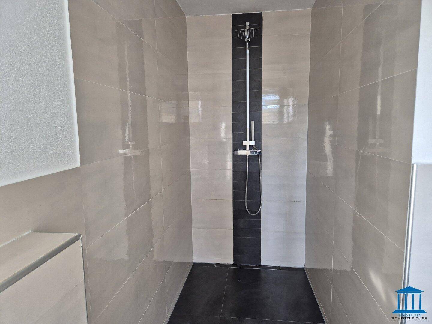 Geräumige begehbare Dusche mit modernen Fliesen in Hell- und Dunkelgrau.