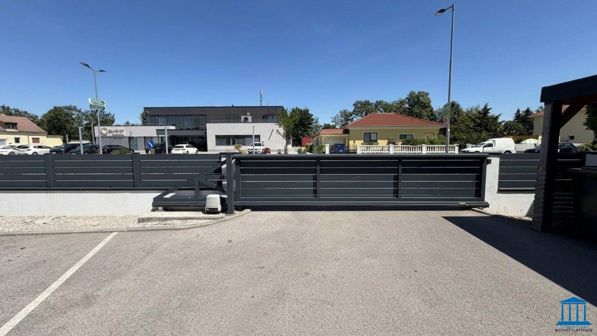 Eingang zum Parkplatz mit einem modernen Schiebetor und umliegender Bebauung.