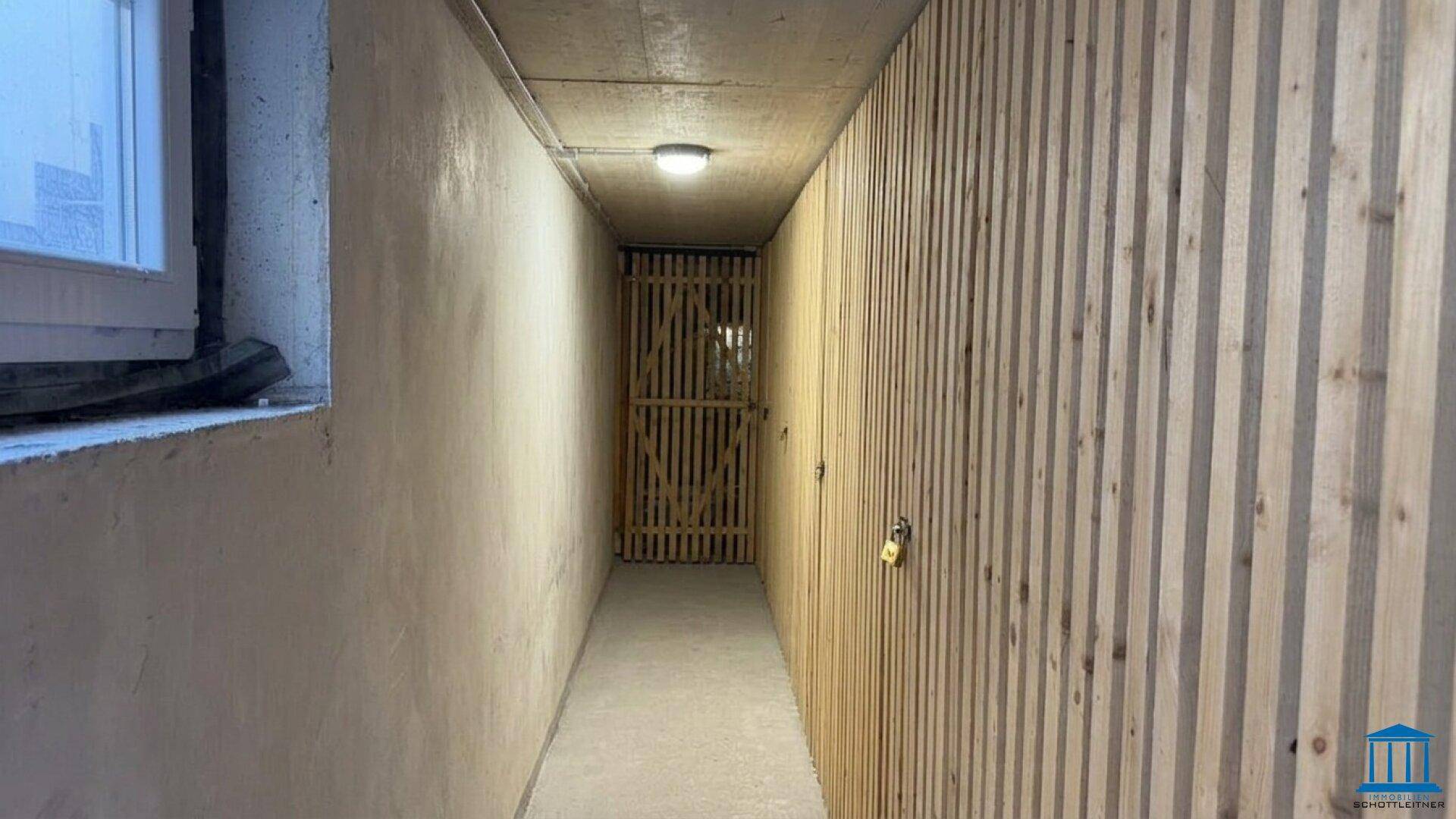 Langer Kellergang mit Holzverkleidung und Fenster, ideal als Abstellraum.