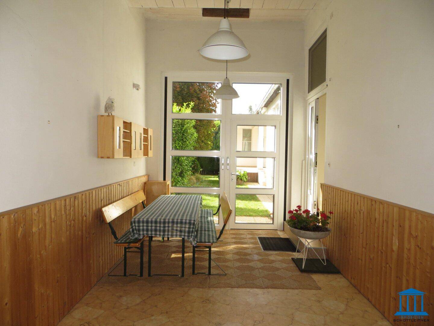 Heller Eingangsbereich mit Holztäfelung und Blick in den grünen Garten durch große Fenster.