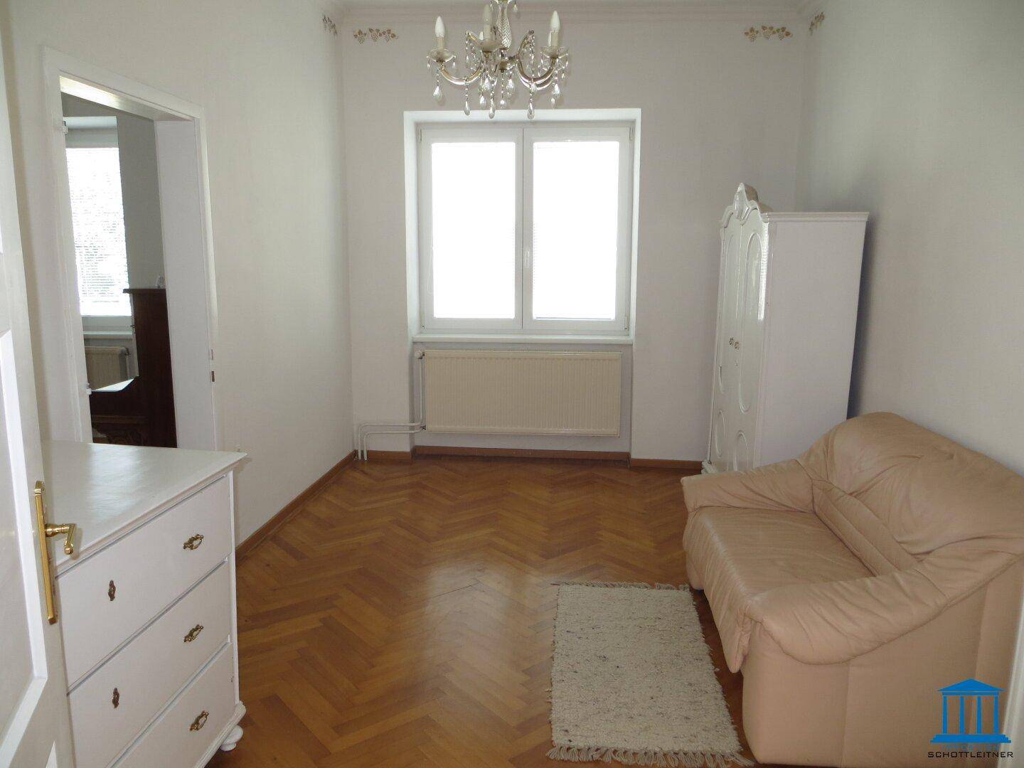Helles Wohnzimmer mit Fischgrätparkett, einem Sofa und einem eleganten Kronleuchter.