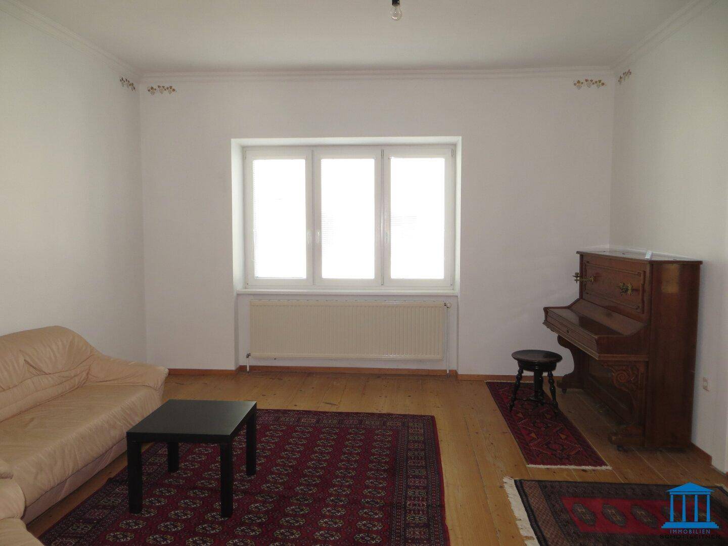 Geräumiges Zimmer mit Holzdielenboden, einem Klavier und großen Fenstern für viel Licht.