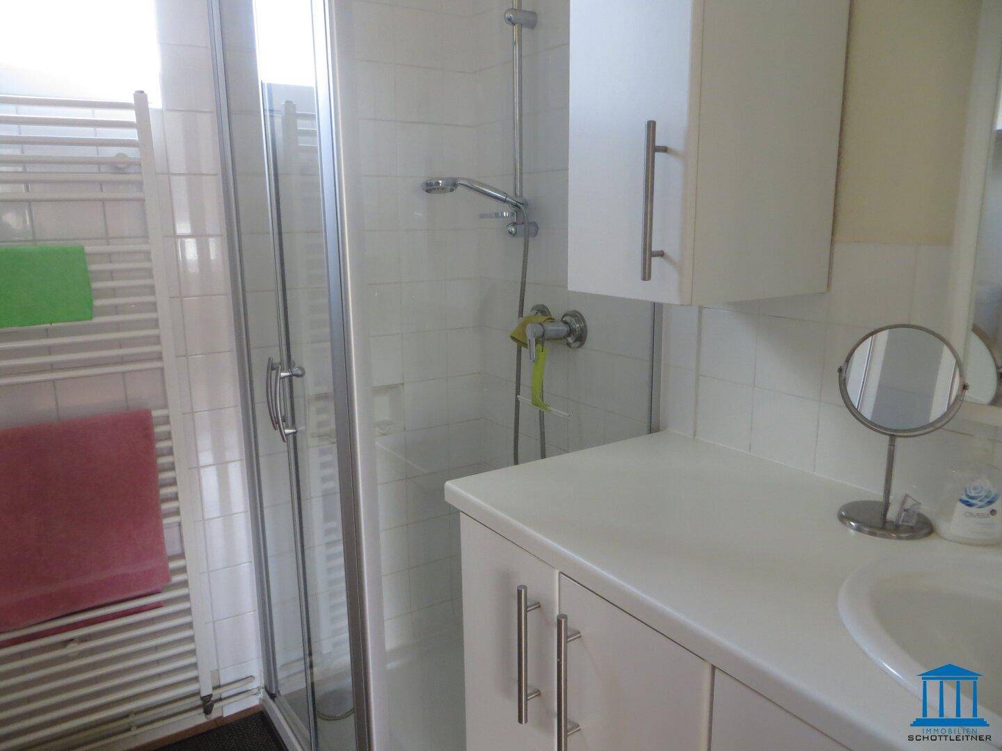 Helles Badezimmer mit Duschkabine, Waschbecken und weißem Heizkörper an der Wand.