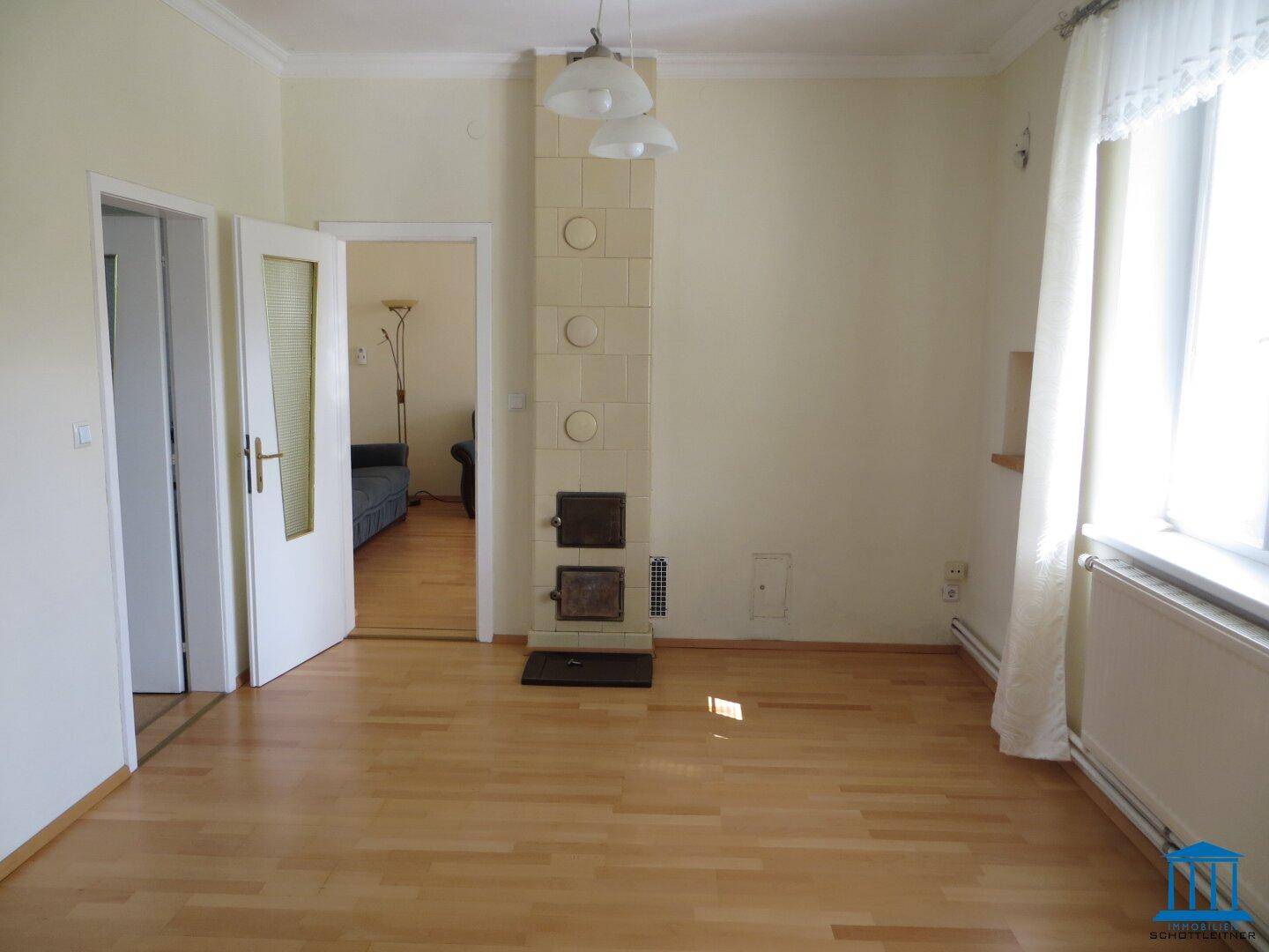 Helles Zimmer mit Parkettboden und einem traditionellen Kachelofen als Heizelement.
