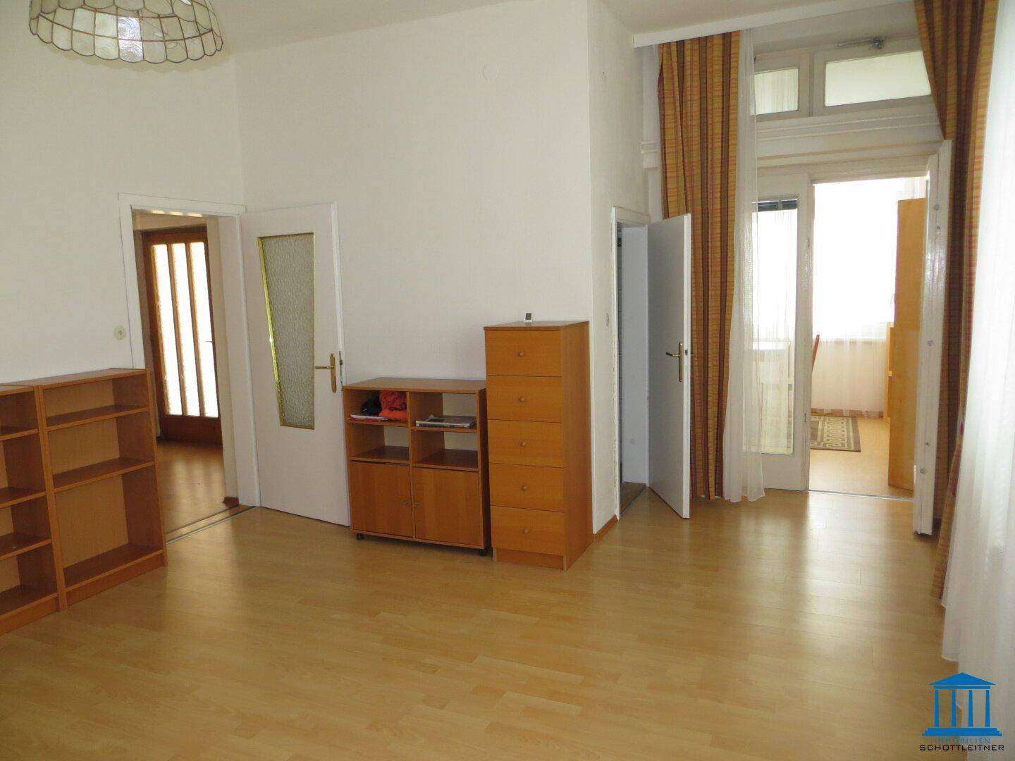 Geräumiges Zimmer mit Parkettboden, Regalen und Zugang zu einem Balkon oder einer Loggia.