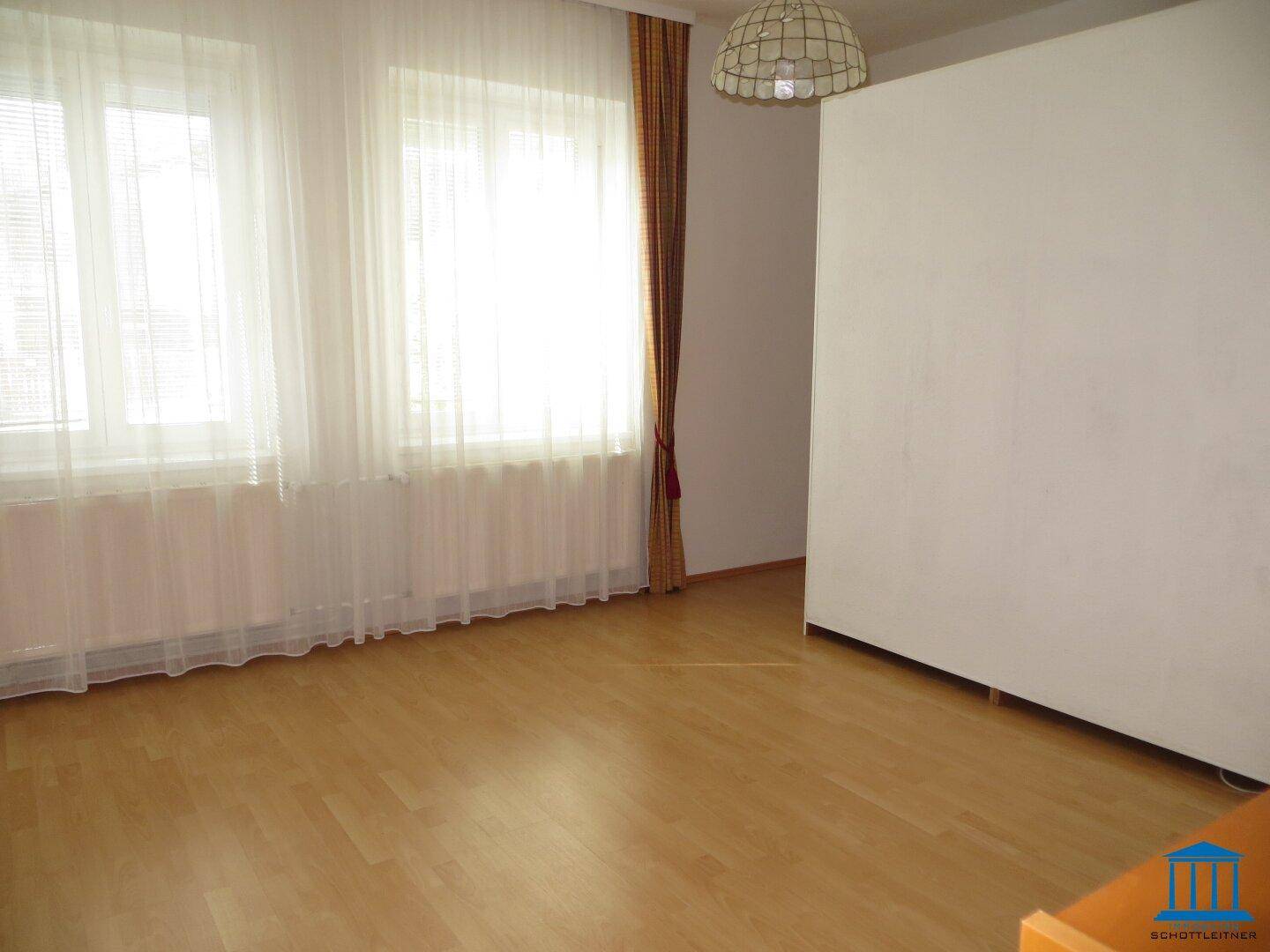 Helles Zimmer mit Parkettboden und einer großen weißen Wand, die den Raum teilt.