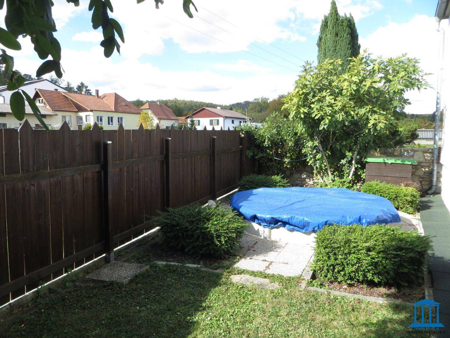 Hinterhof mit einem abgedeckten Pool und einem Holzzaun, umgeben von Büschen und Rasen.